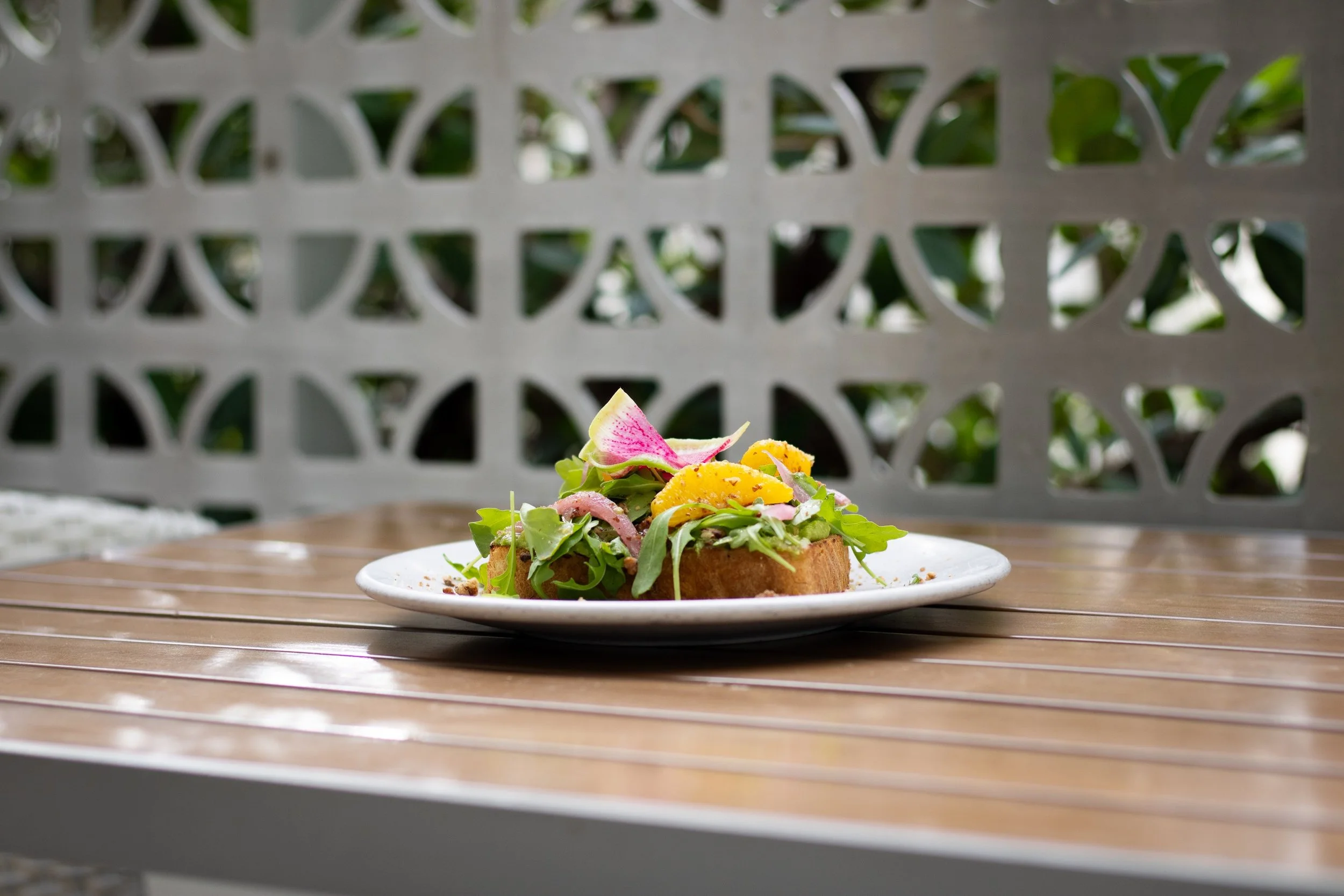 Plate of salad with greens, sliced yellow fruit, and other vegetables on a wooden table outdoors.