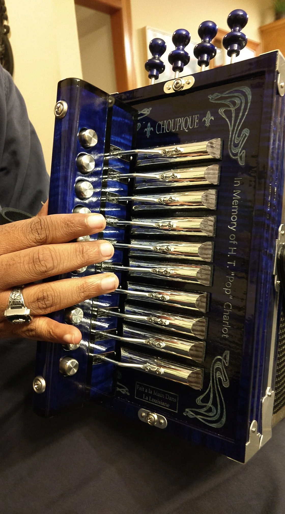 A person pressing the buttons of a choupique blue accordian with metallic accents and decorative designs.