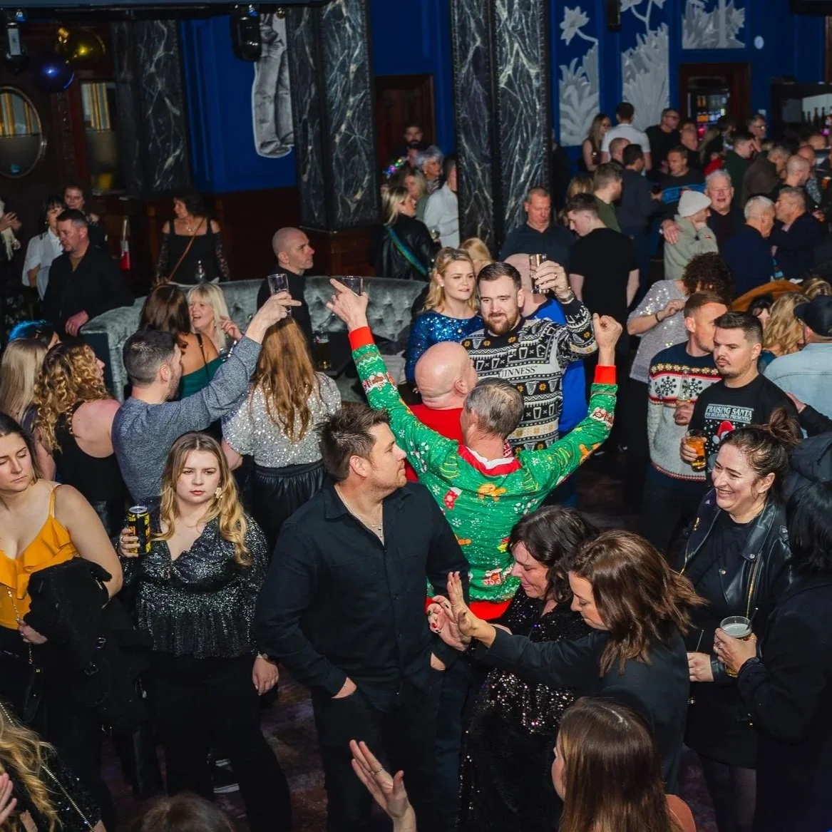 People celebrating at a holiday party, dancing and raising glasses in a festive atmosphere.