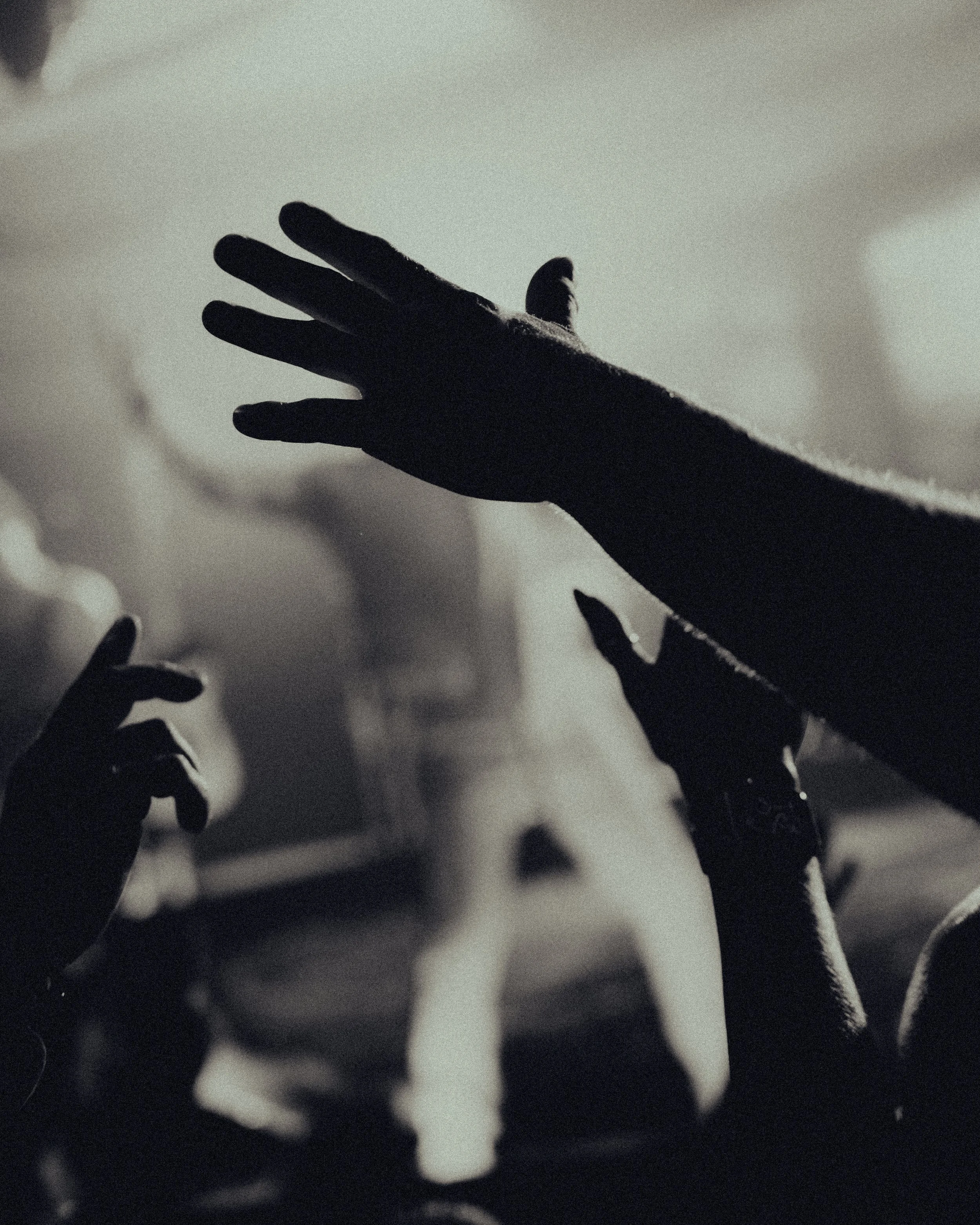 Silhouetted hand reaching upward, with other hands in the background, creating a dramatic and artistic scene.