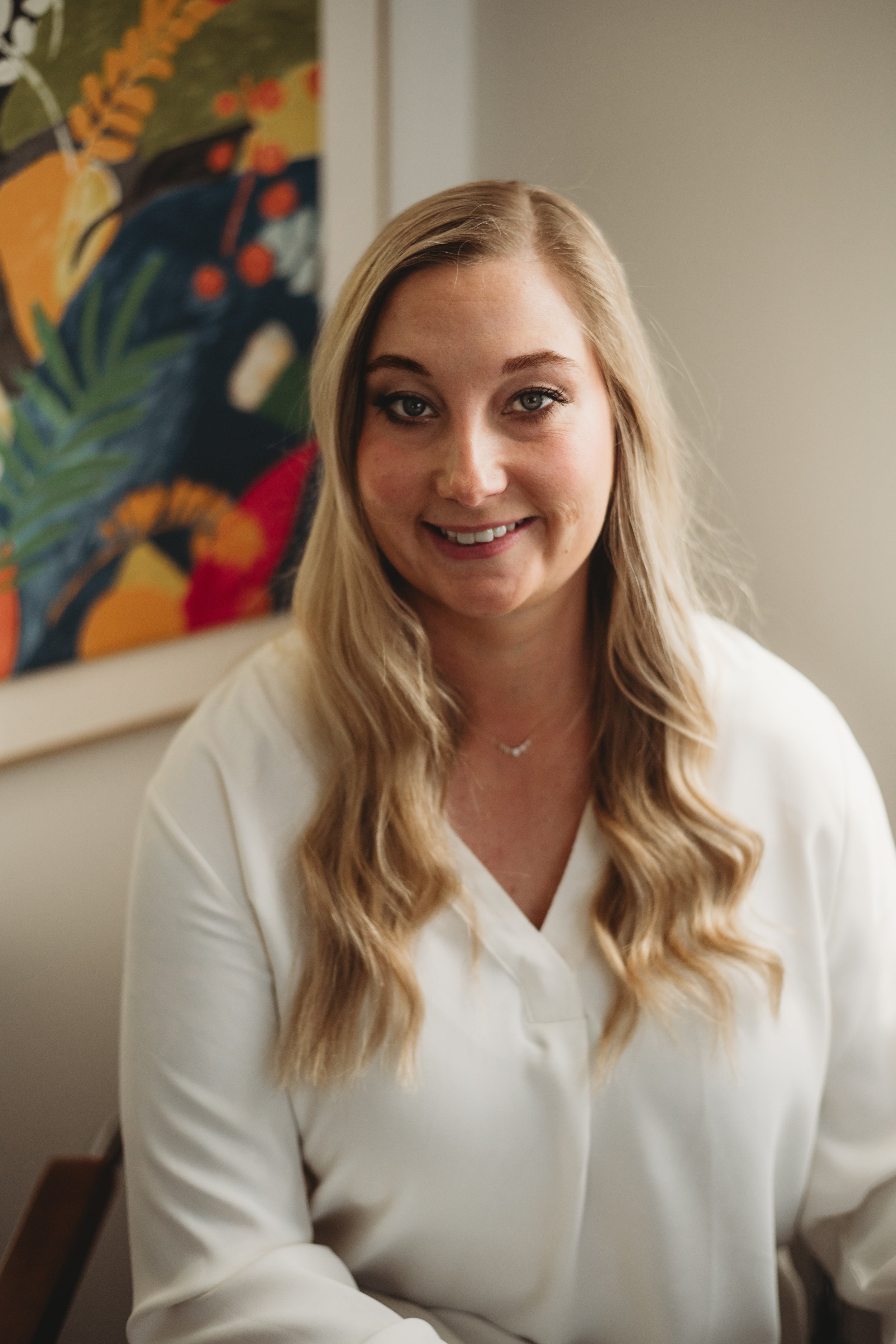 Kelsey Mammen, North Longmont, Colorado therapist, sitting in her in-person office with colorful painting