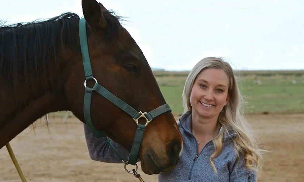 Kelsey Mammen, outside, standing next to her horse, smiling, getting ready for an Equine-Assisted Therapy session .png