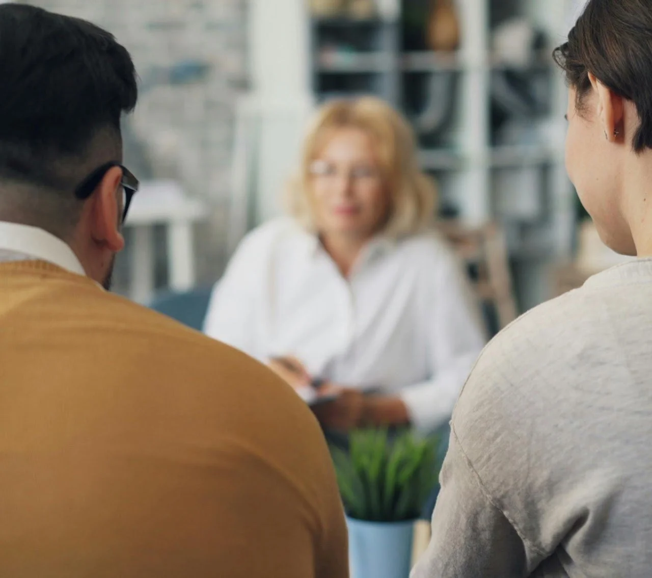 Two men sitting in front of a woman, who is blurred in the background, in a casual meeting or discussion setting.