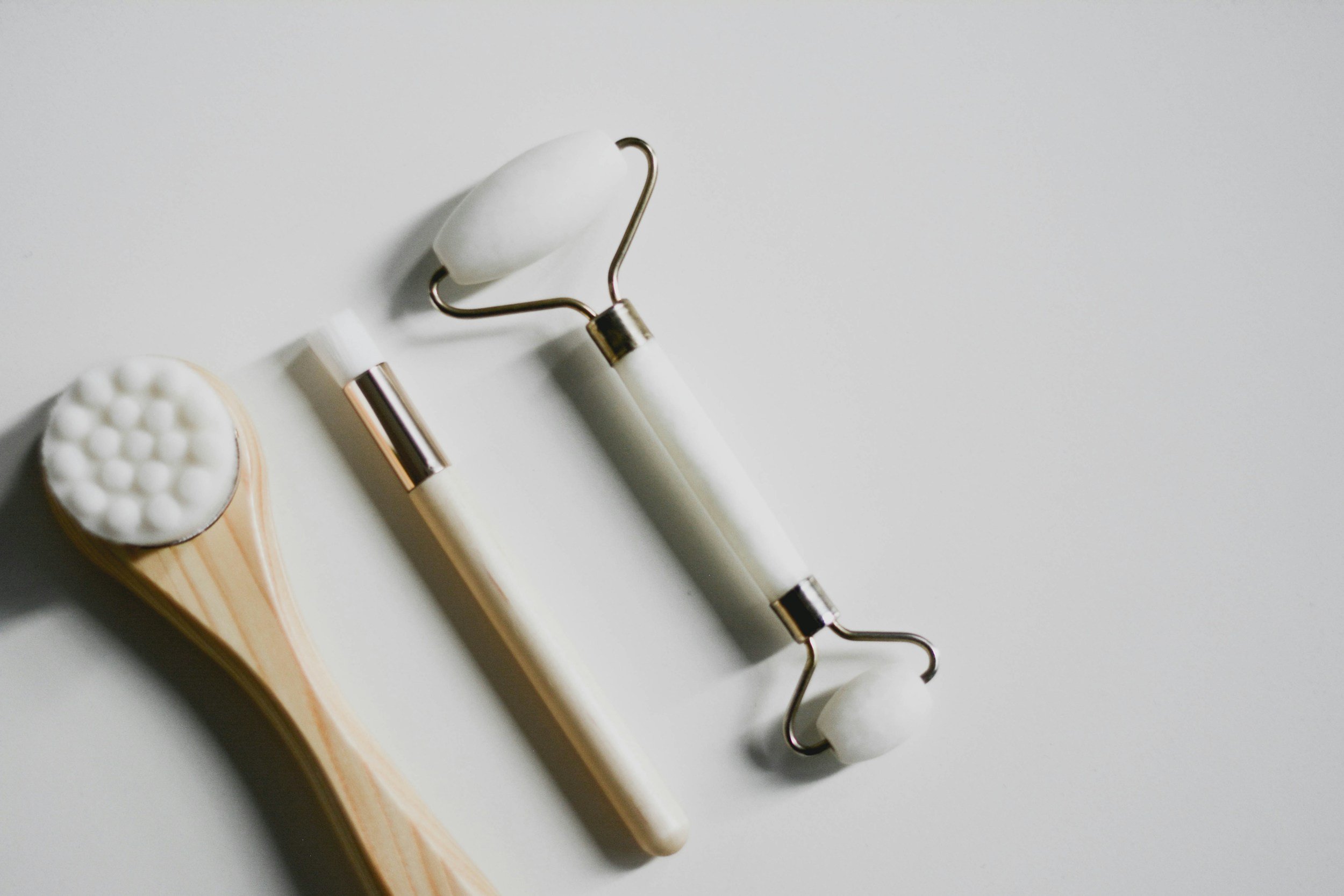 A facial roller, a gua sha tool, a jade roller, and a massage roller, all skincare tools, arranged on a white surface.