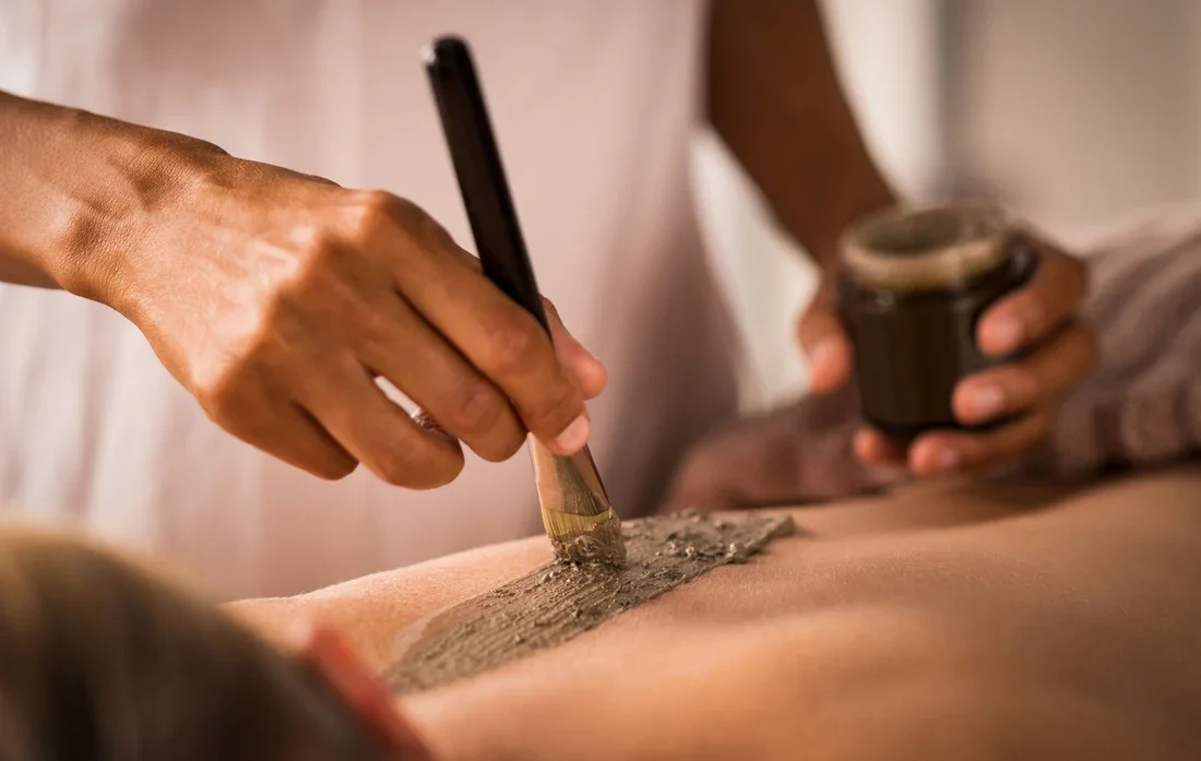 A person applying tattoo ink with a brush to a tattoo on someone's skin while holding a cup of ink.