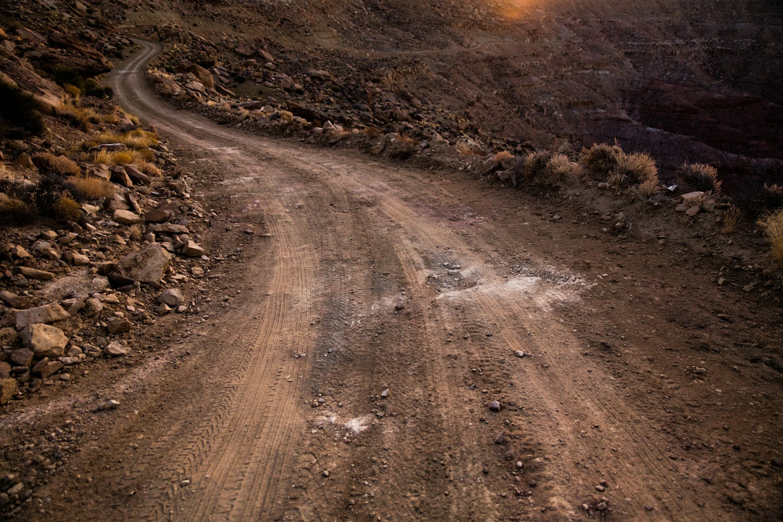 A dirt mountain road winding through a barren, rocky landscape