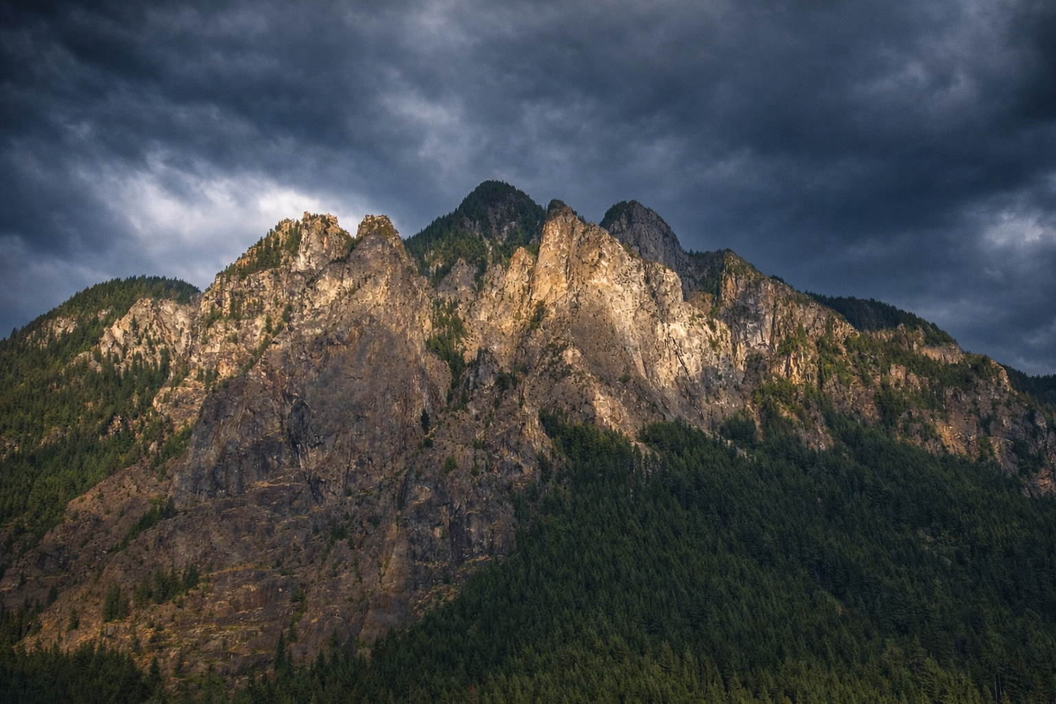 "Breaking Through"
The mountain rises into shadow and light, cutting through what gathers above it. Elevation isn’t given—it’s forced.