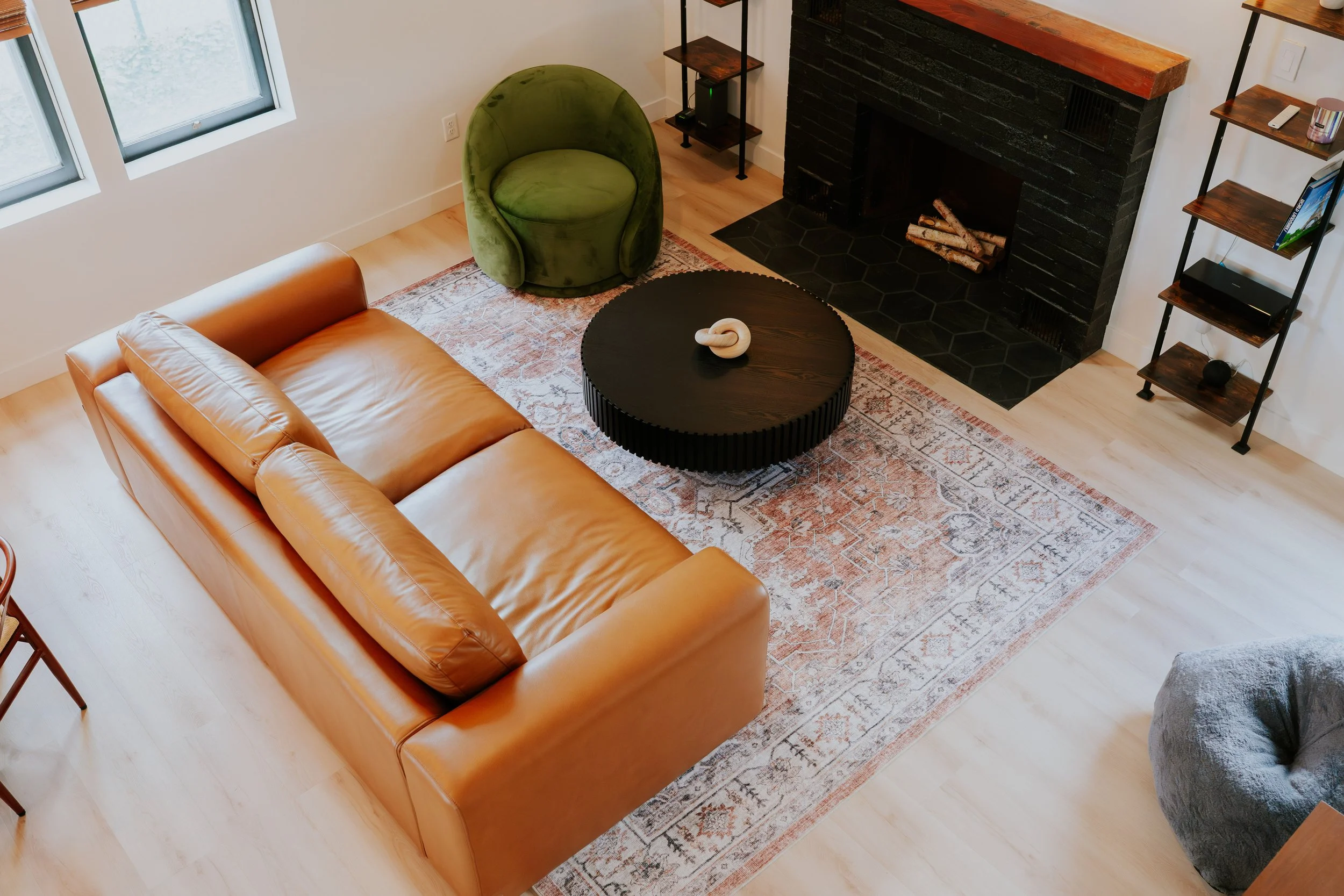 Living room with tan leather sofa, green armchair, black fireplace, wooden shelves, and window