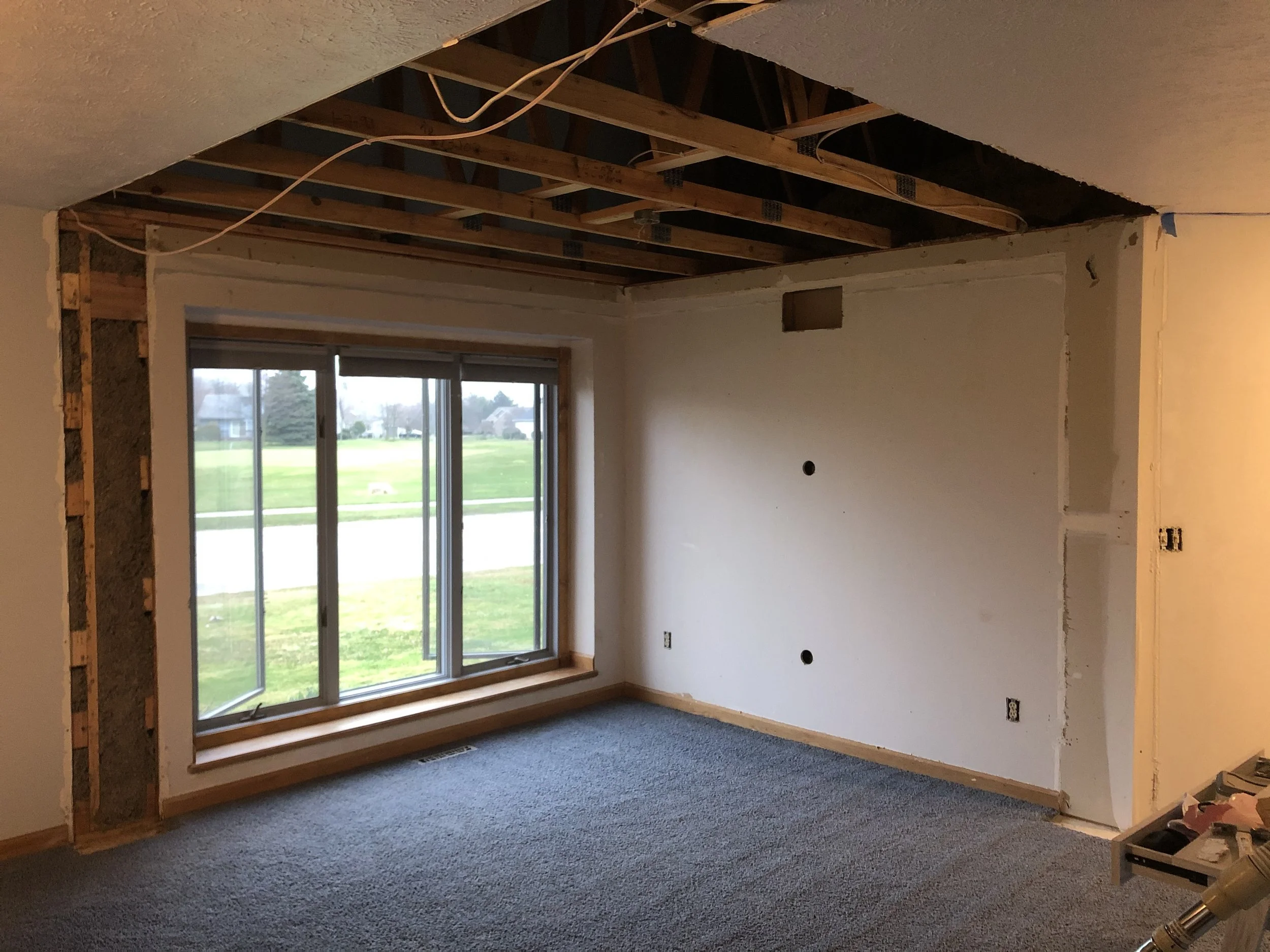 Room under renovation with exposed ceiling beams, a large window, and partially painted walls.
