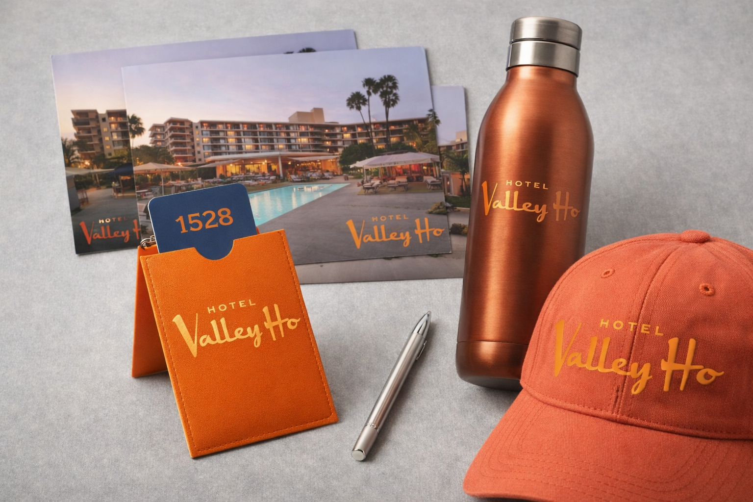 Hotel Valley Ho branding items including postcards, a metal water bottle, a hat, a pen, and a room key card with the hotel’s pool and building in the background.