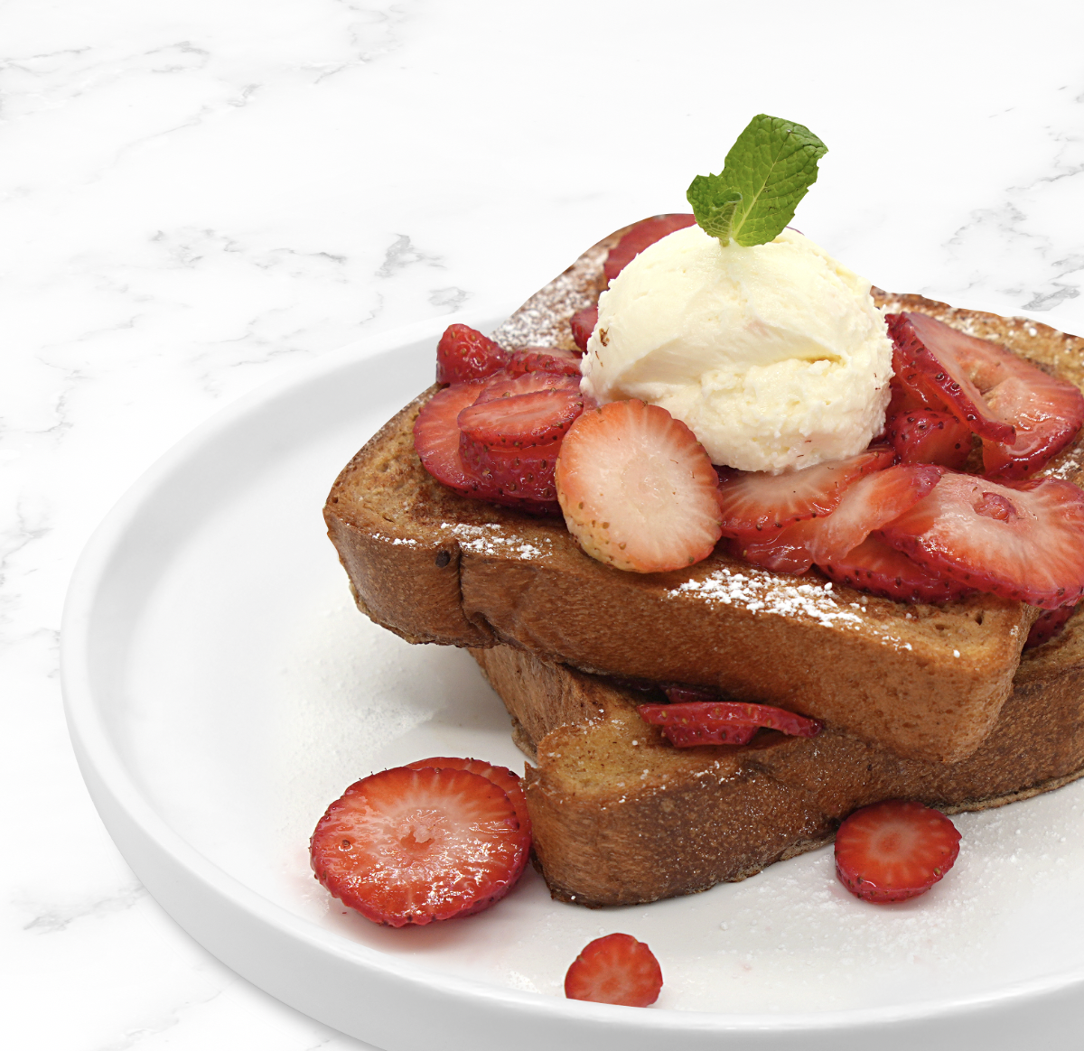 French toast topped with sliced strawberries, a scoop of vanilla ice cream, and a mint leaf on a white plate.