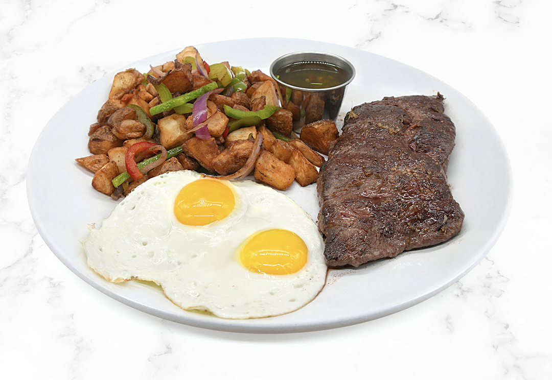 Breakfast plate with two fried eggs, roasted potatoes with vegetables, a serving of cooked steak, and a small cup of sauce or gravy.