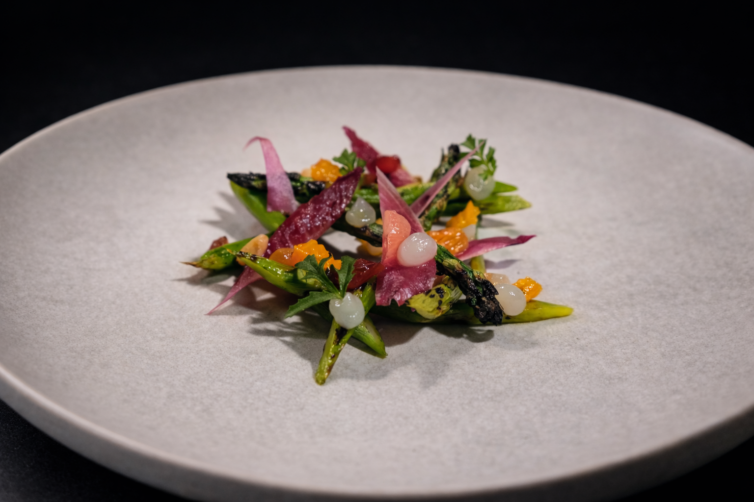 A gourmet plated dish with colorful vegetables and garnishes on a light gray plate.