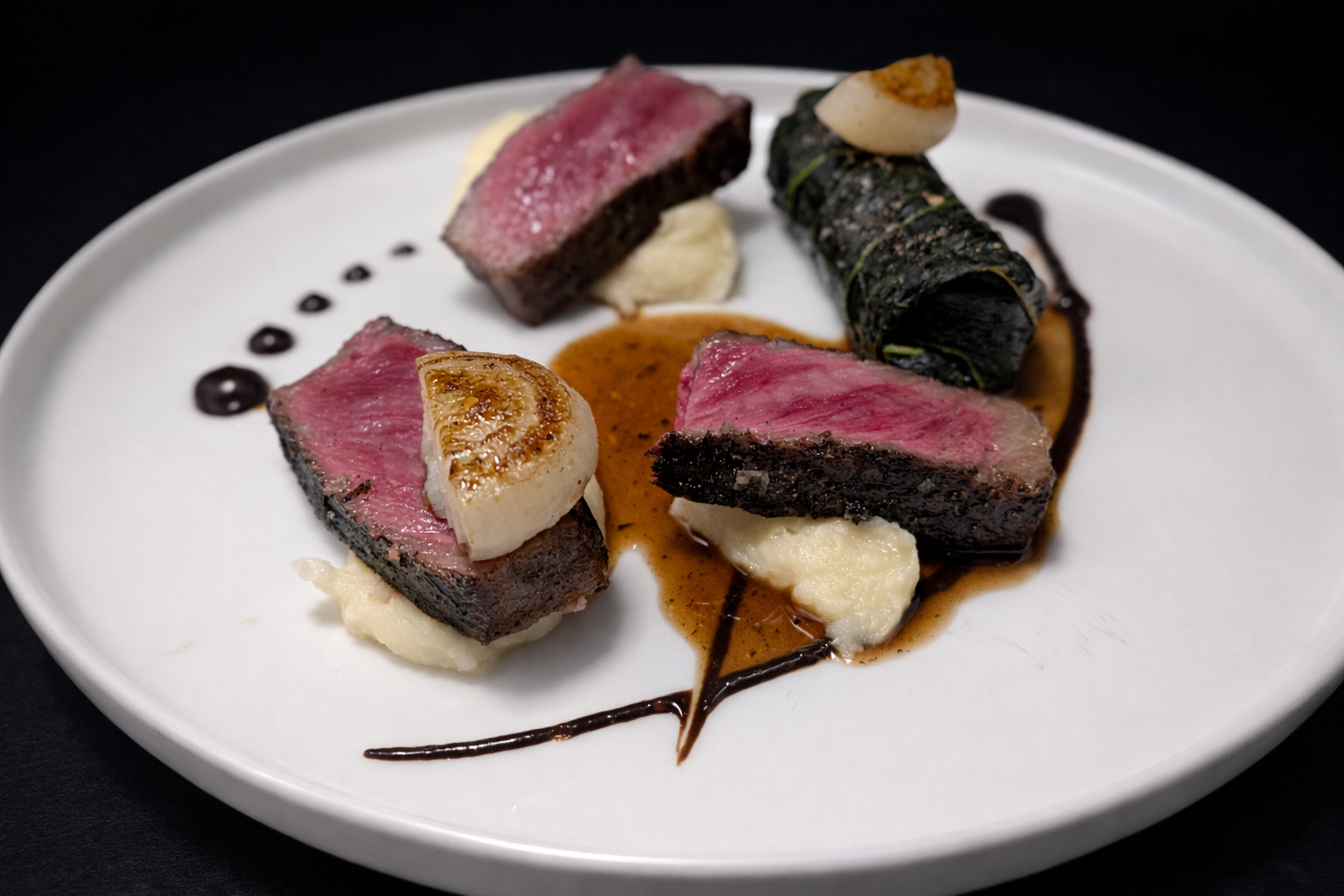 Close-up of a gourmet dish with medium-rare steak slices, seared scallops, a seaweed wrap roll, mashed potatoes, dark sauce, and decorative sauce dots on a white plate.