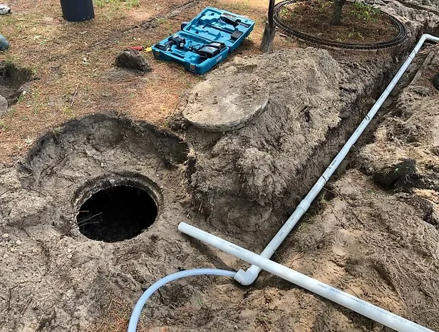 A backyard outdoor scene with a trench and PVC pipe plumbing installation, a blue toolbox on the ground.
