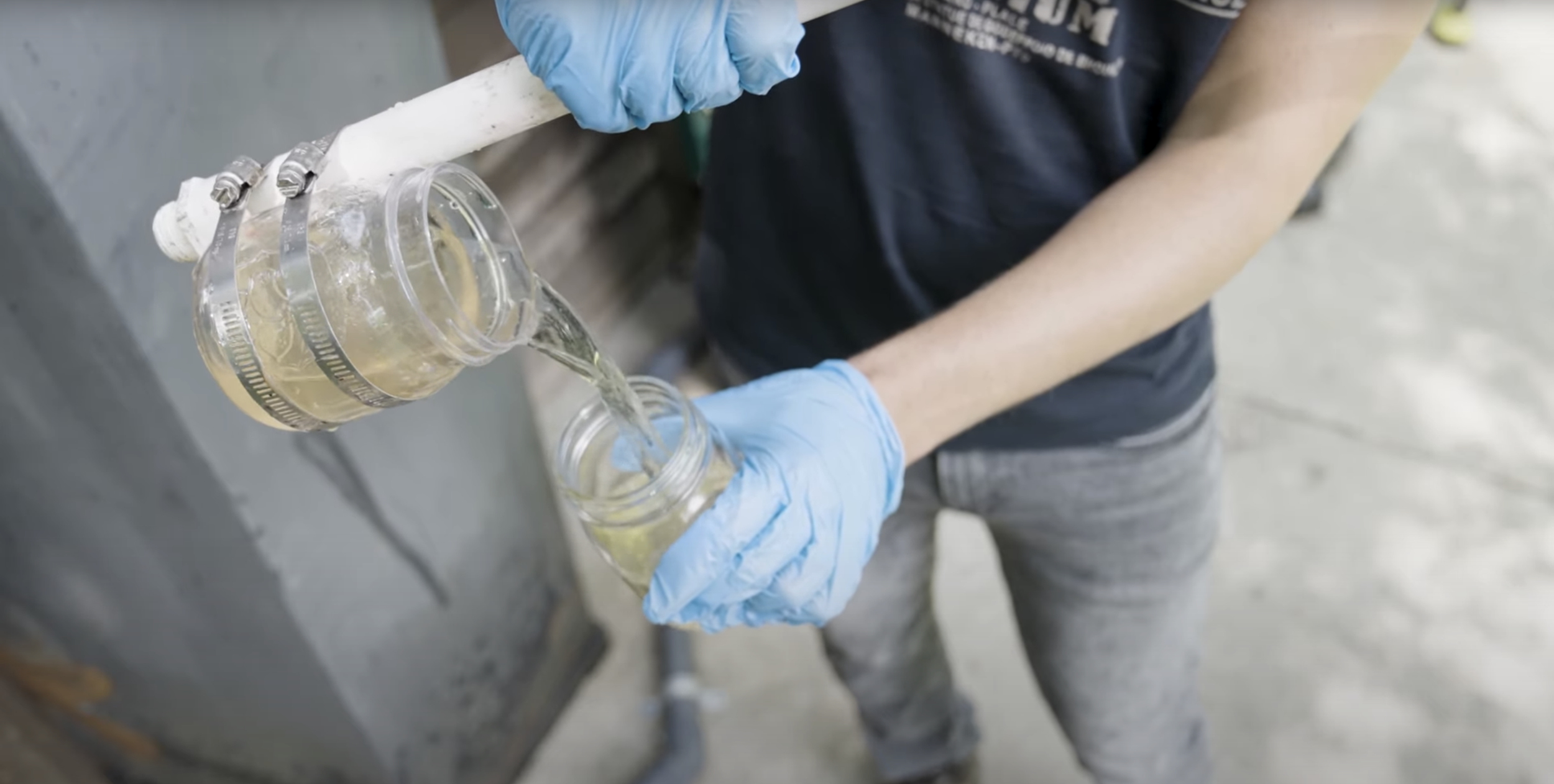 A person wearing blue gloves pours clear water treated by IMET Technology into a jar after