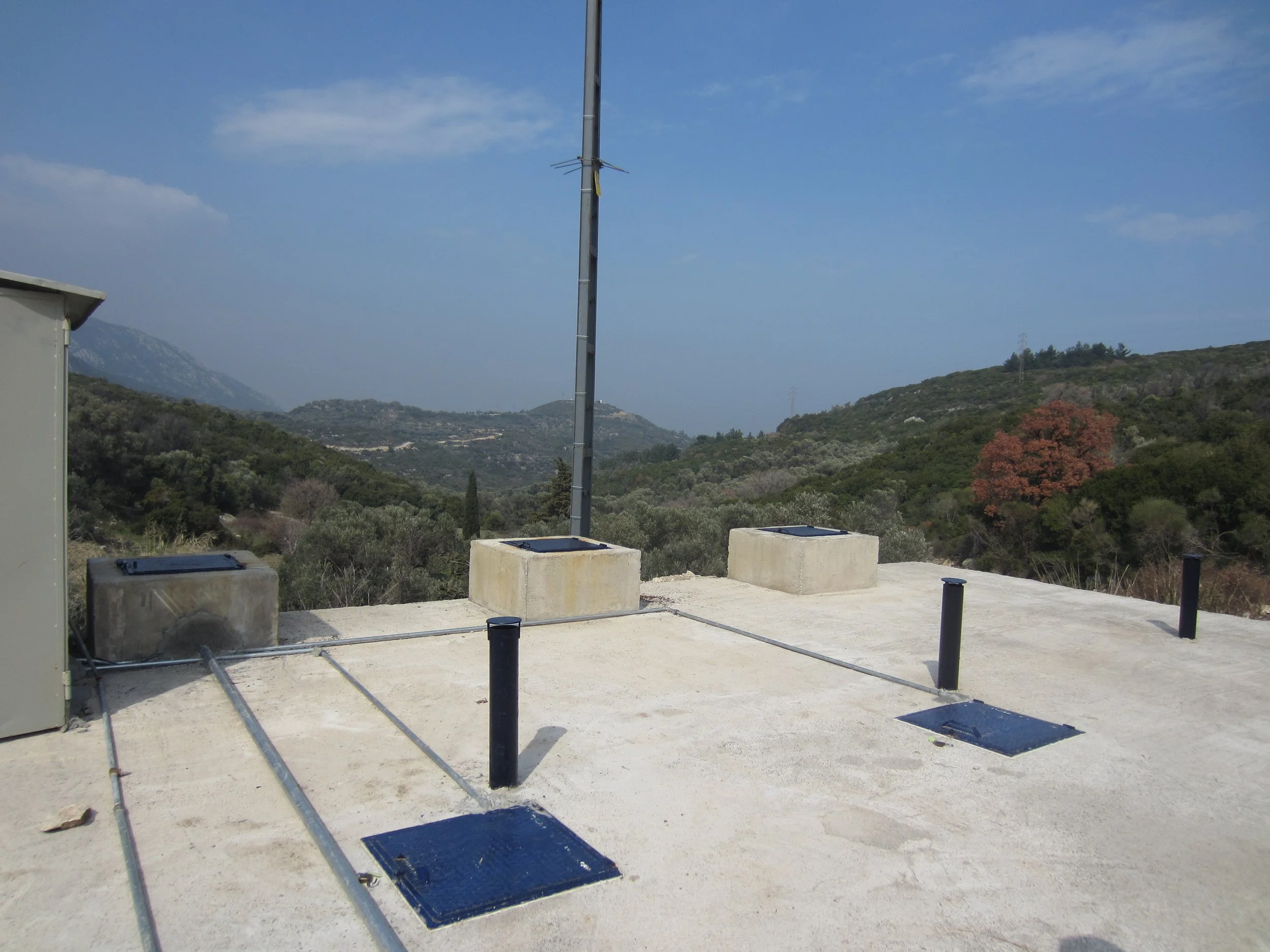 Wastewater treatment plant overlooking green hills and mountains in the distance under a blue sky with scattered clouds.