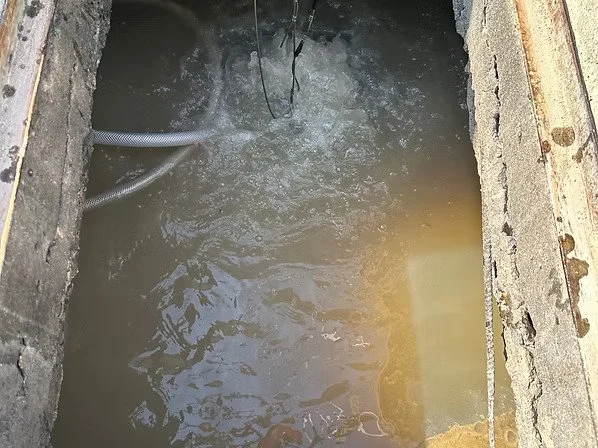 A rectangular concrete pool with river-colored water and some hoses or pipes inside.