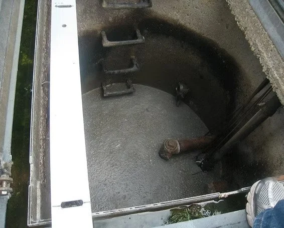 An open underground utility vault or manhole with thick bio-mat buildup