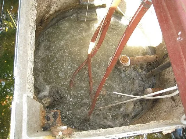 An open underground utility vault or manhole with river-colored water bubbling