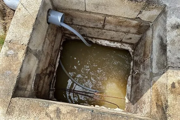 A rectangular stone well filled with river-colored water, with a gray water pump and hose attached to the side.