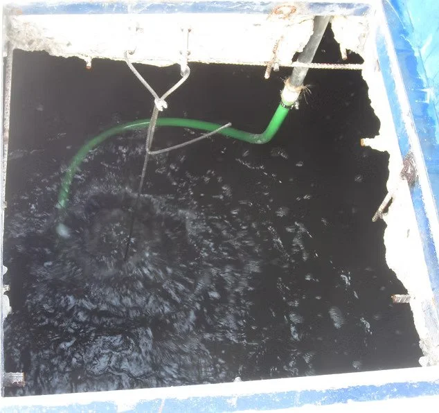 Close-up of a sewer or drain with lightly bubbling water and green piping visible.