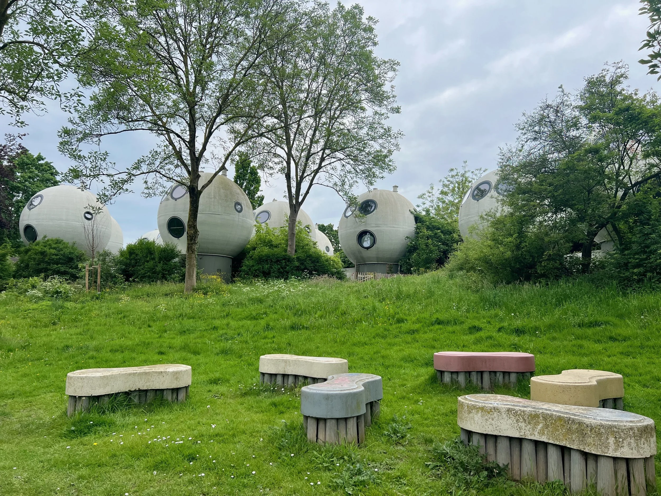 Bolwoningen homes in 's-Hertogenbosch surrounded by  green grassy area with colorful stone benches.  The futuristic spherical buildings with circular windows provide views of nearby canals and bike pathways.