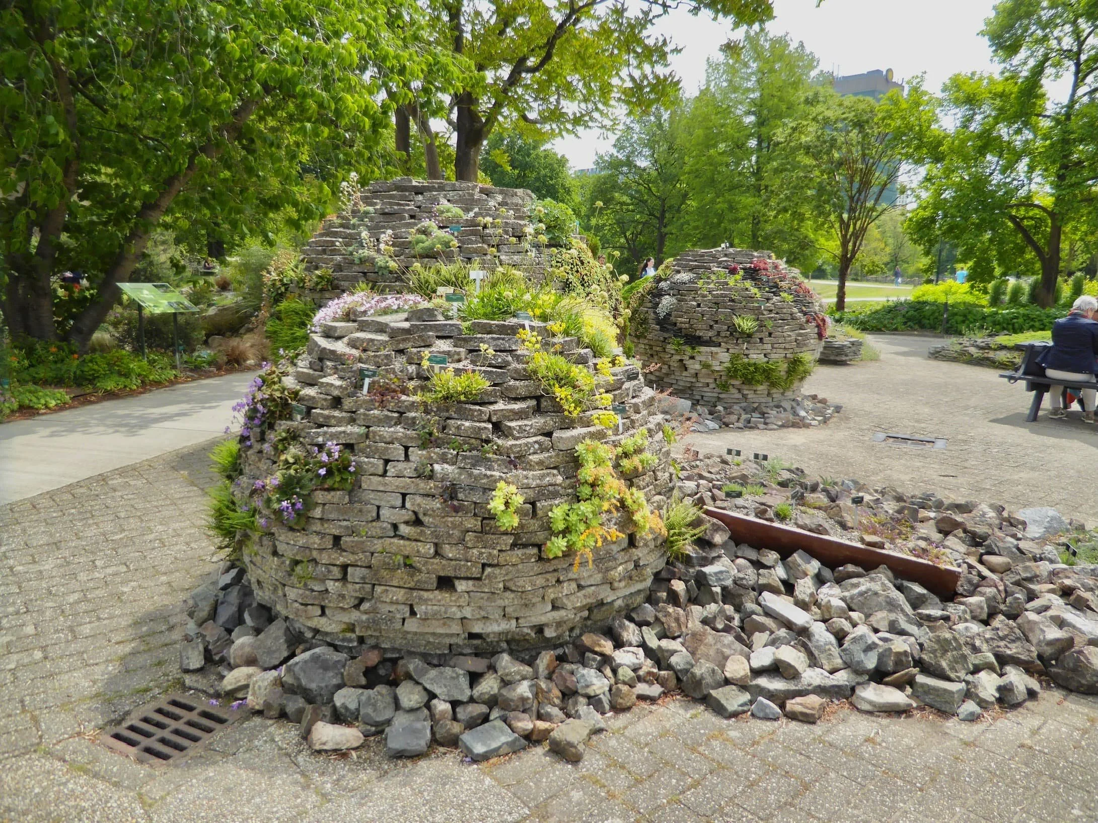 Three large spherical stone crevice garden structures with plants growing on and around them are located in Utrecht Botanic Garden.