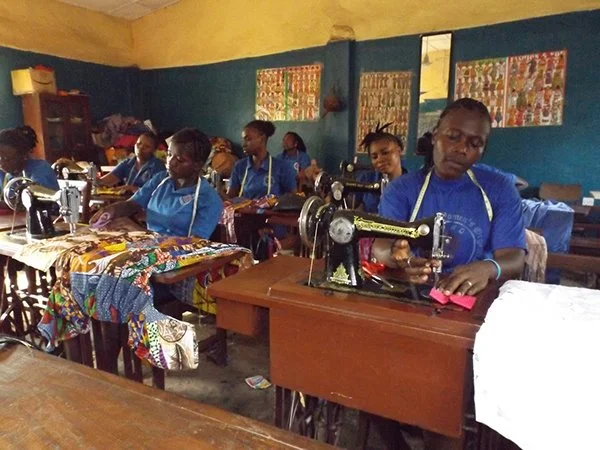 Group of women in blue uniforms working with sewing machines in a classroom.