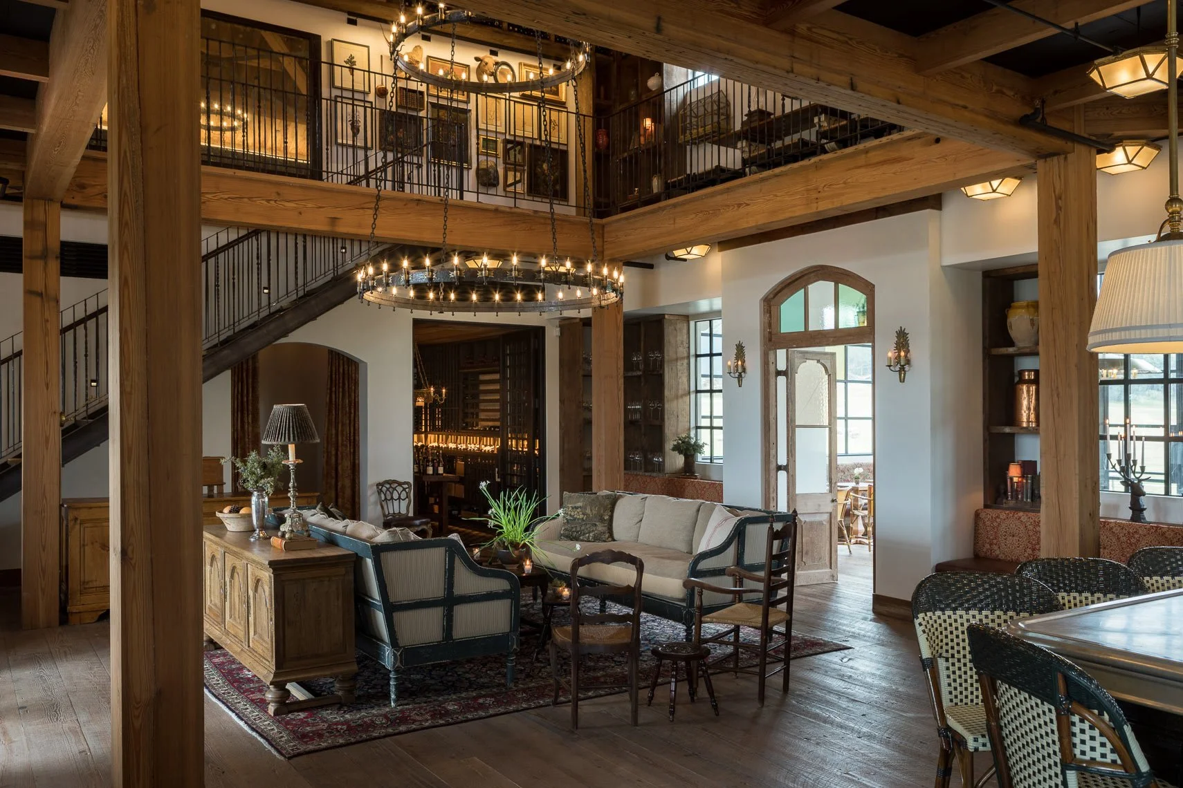 Interior of a rustic style living room with wooden beams, chandelier, sofa, armchairs, and decor items like vases and paintings.