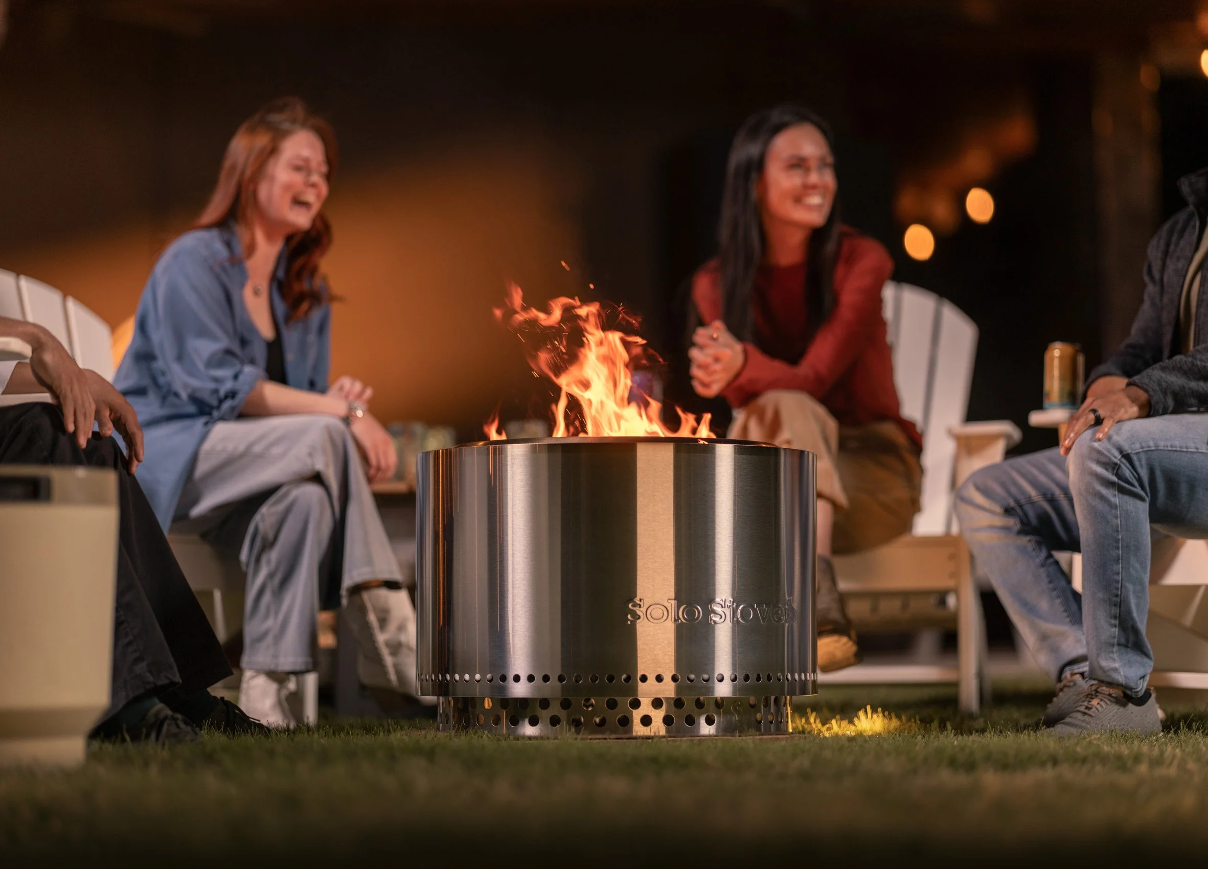 People sitting around a bonfire at night, enjoying a social gathering.