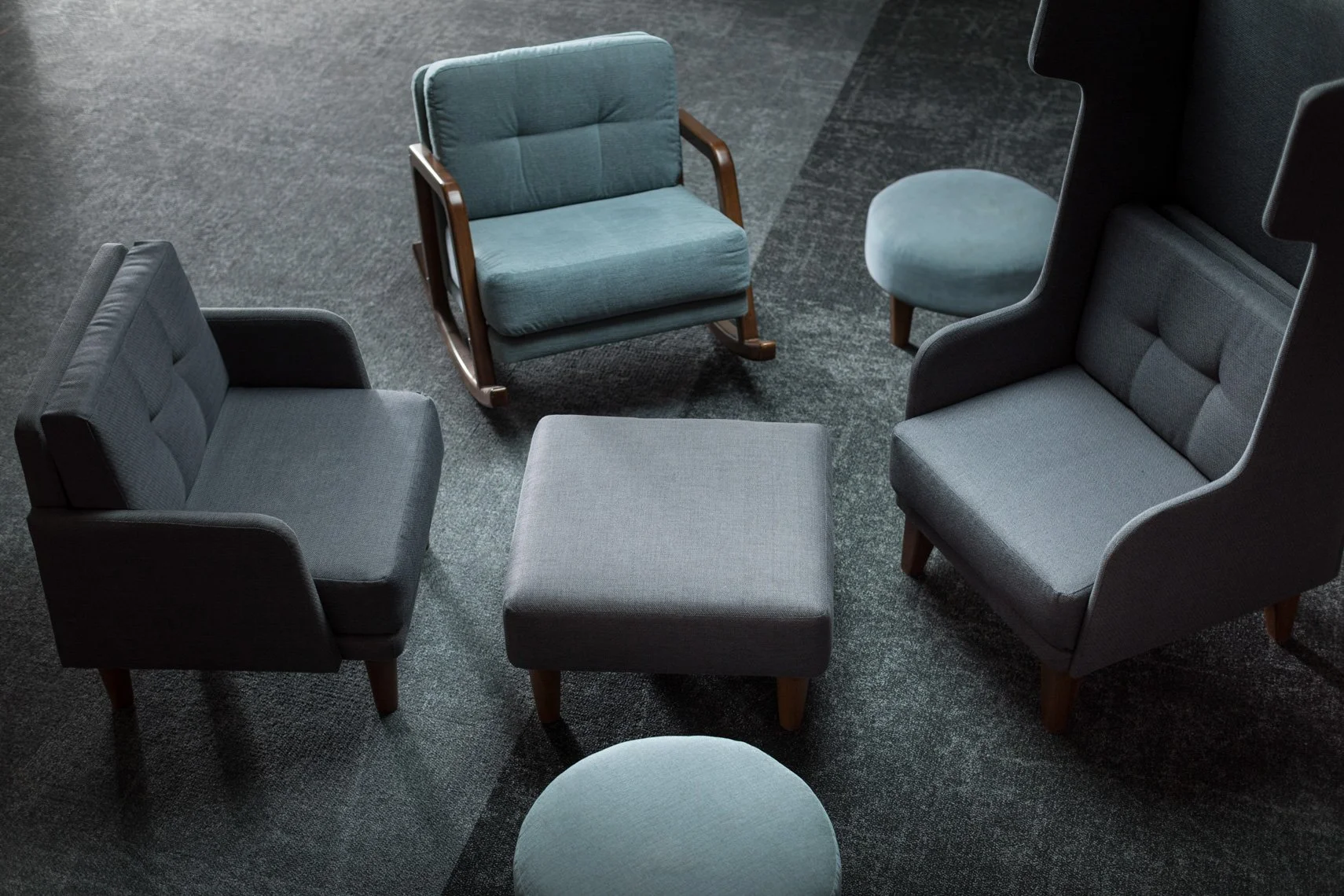 A group of six vintage-style chairs arranged in a circle with a small round ottoman in the center on a dark grey carpet.