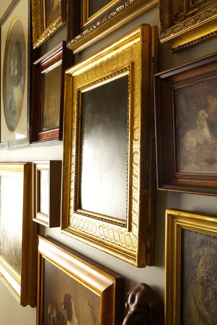 Wall with multiple framed paintings and pictures of various sizes in an art gallery or museum.