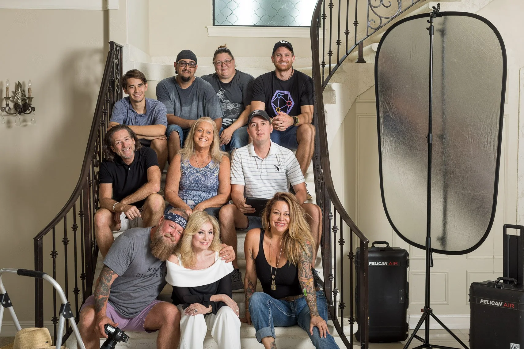 Group of ten people posing on a staircase for a photo, with professional photography equipment such as a reflector and lighting in a home setting.