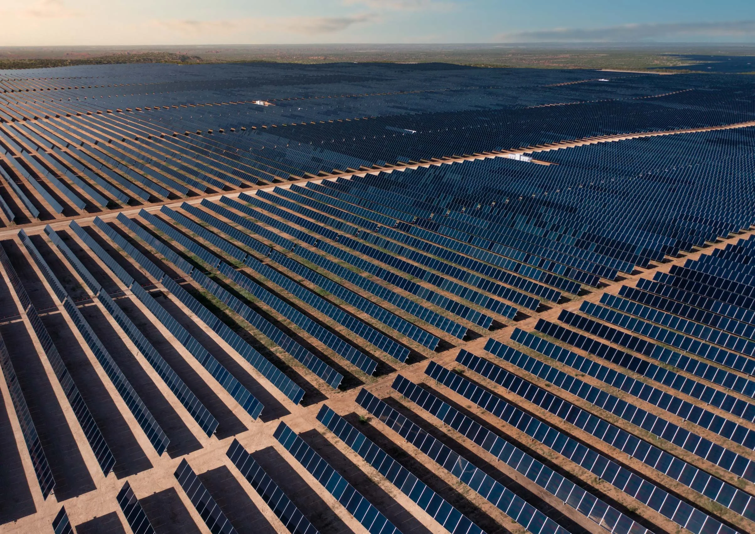 A large solar panel farm located in an open terrain, with numerous rows of solar panels extending towards the horizon.