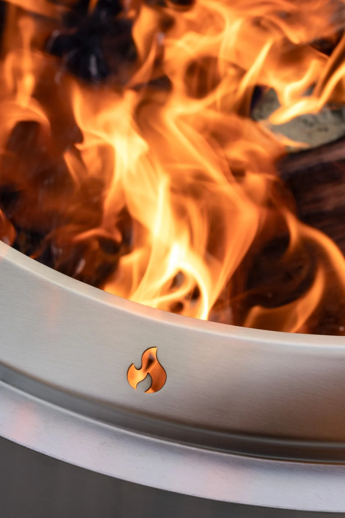 Close-up of a fire burning inside a modern, sleek, metallic fire pit with a small flame cutout on the rim.