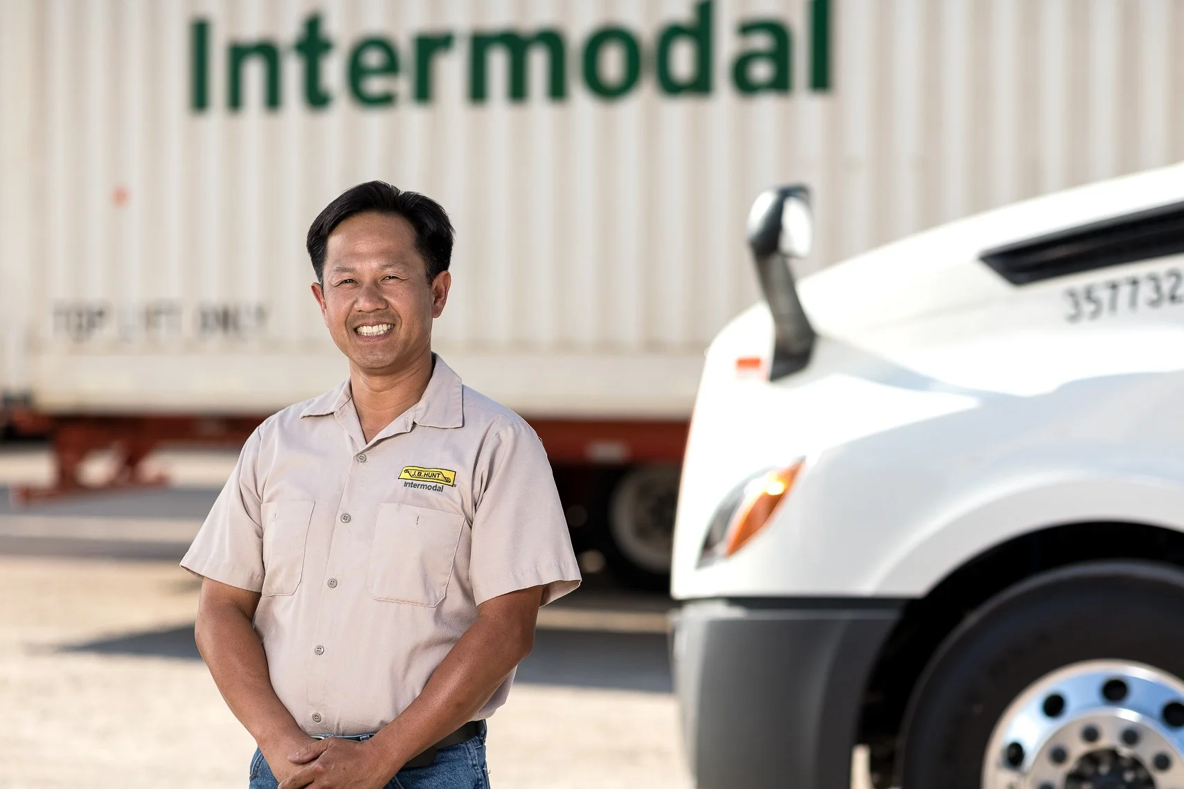 A man wearing a beige work shirt with a name tag and the word 'Intermodal' standing in front of trucks, smiling and looking at the camera.