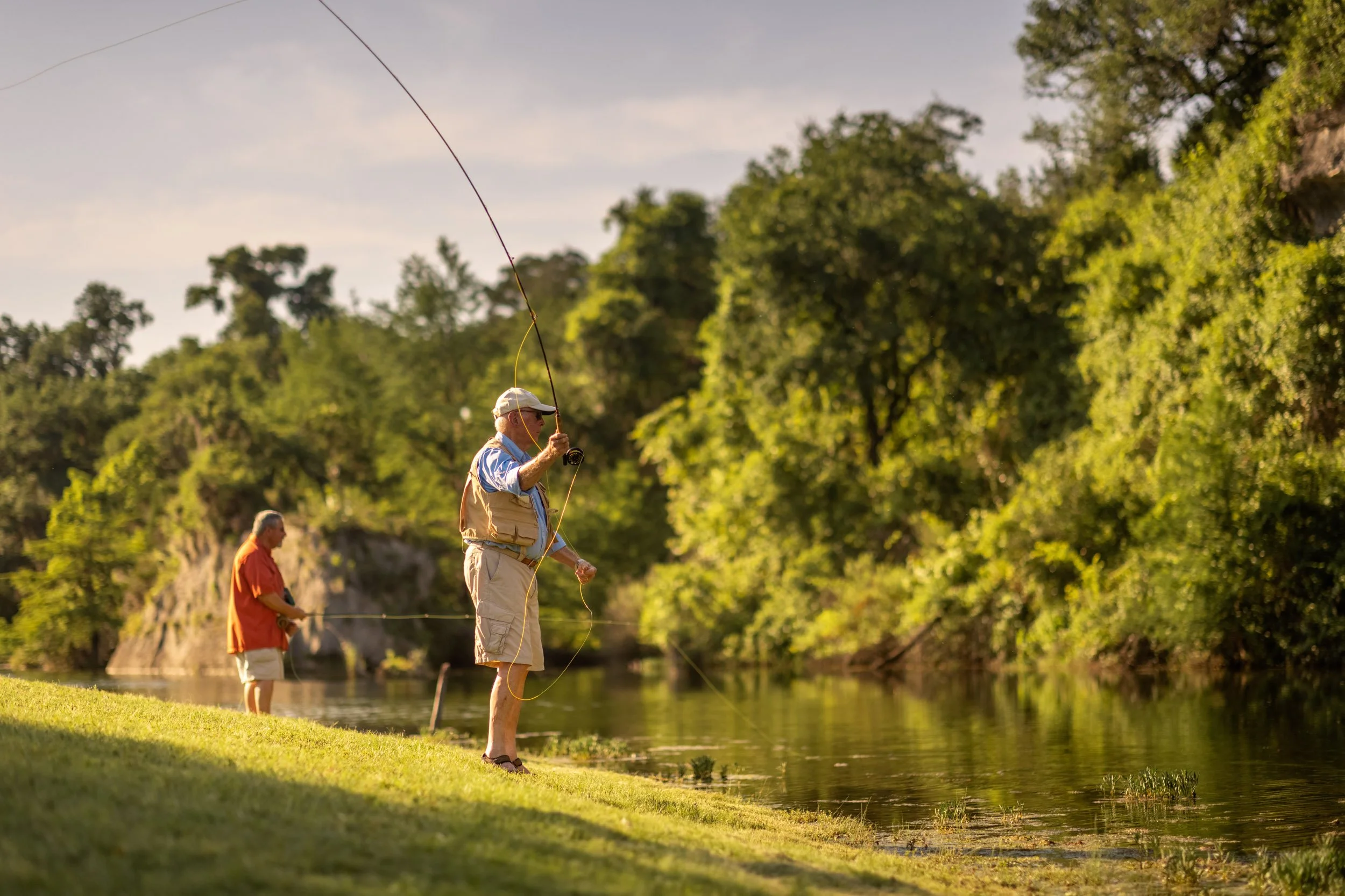 People fishing by a river in a lush green outdoor setting during daytime.