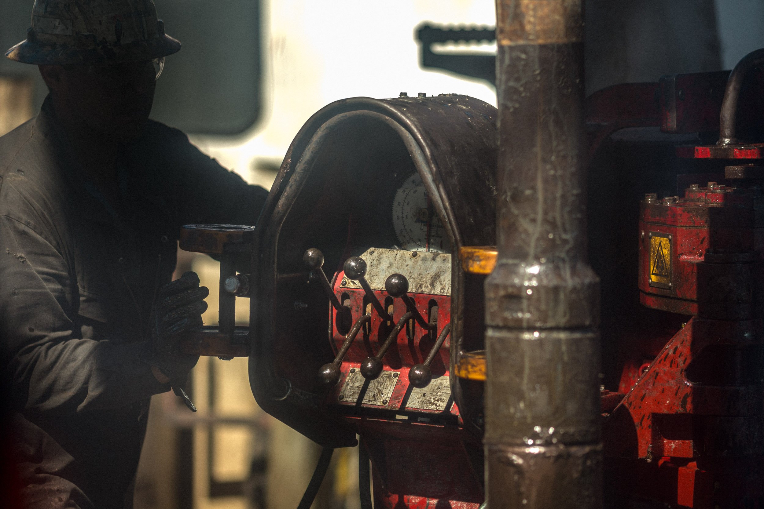 A worker in a hard hat operates industrial machinery in a factory setting.