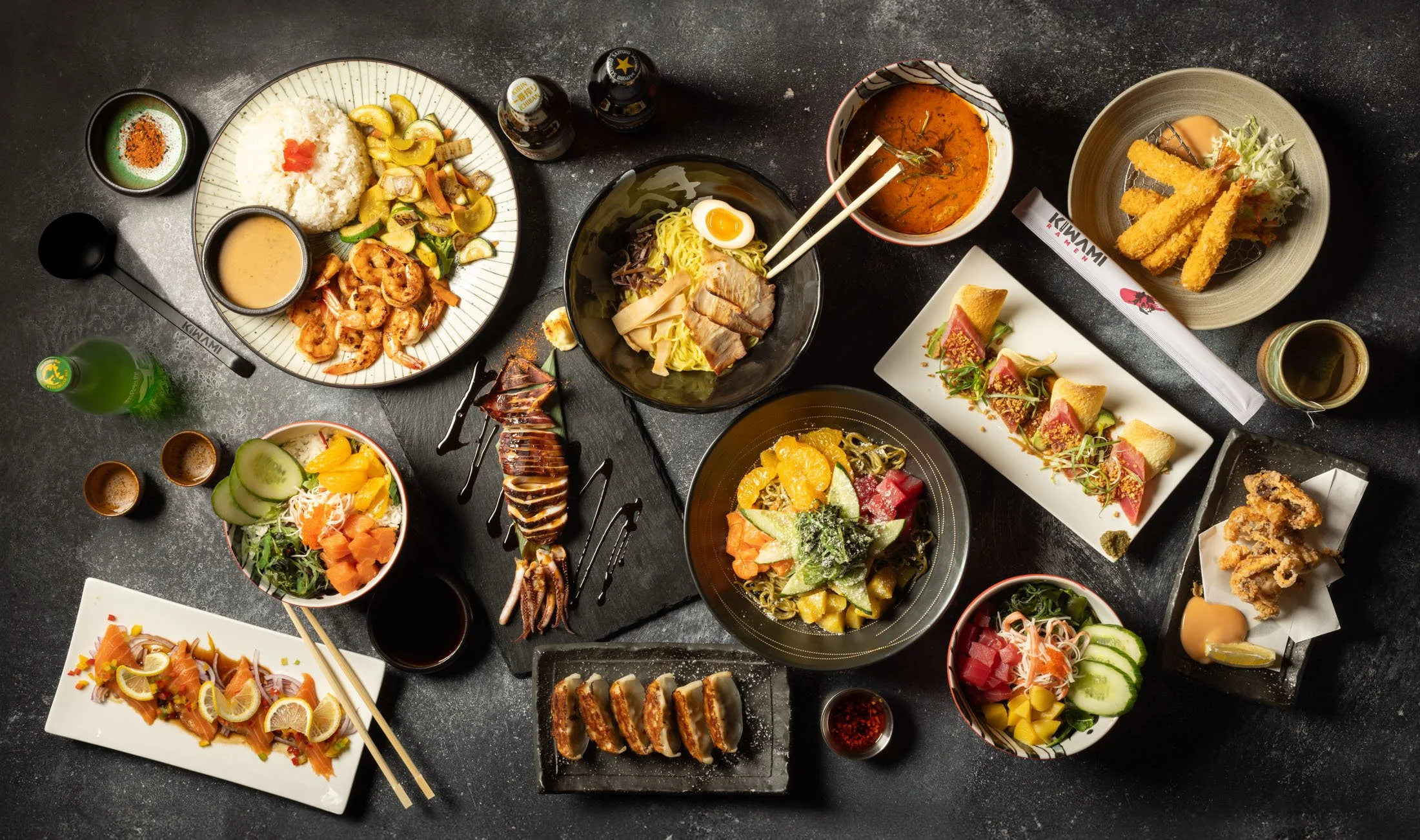 Assorted Japanese dishes including sushi, sashimi, ramen, tempura, salads, and sauces arranged on a black table.