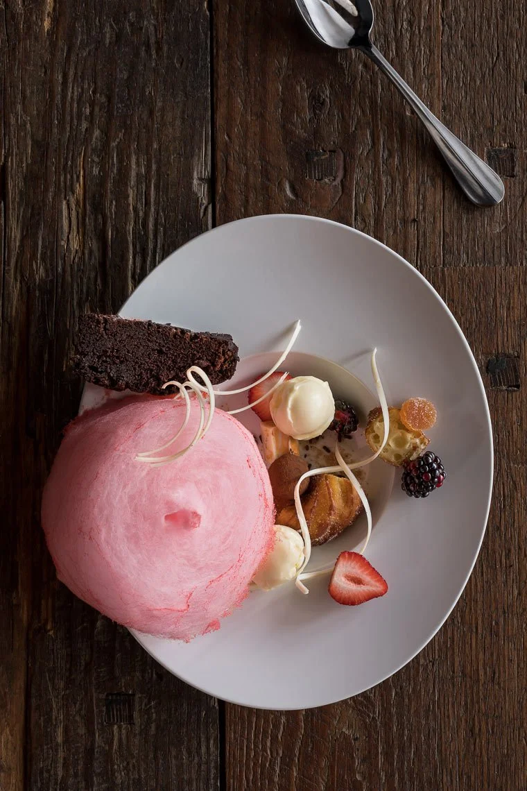 Dessert plate with pink cotton candy, chocolate cake slice, vanilla ice cream, strawberries, blackberries, and small pastries on a white plate