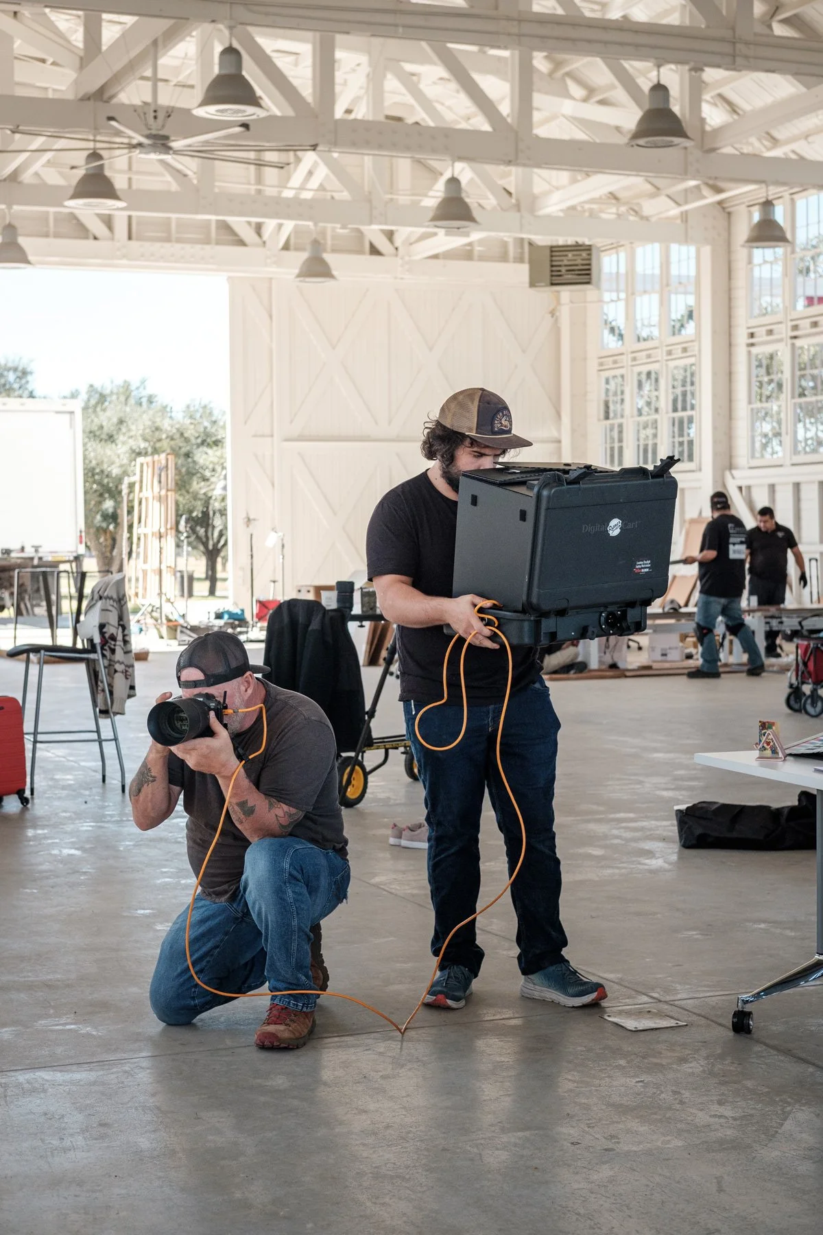 Two men working with professional photography equipment inside a large, well-lit indoor space, possibly a studio or warehouse.
