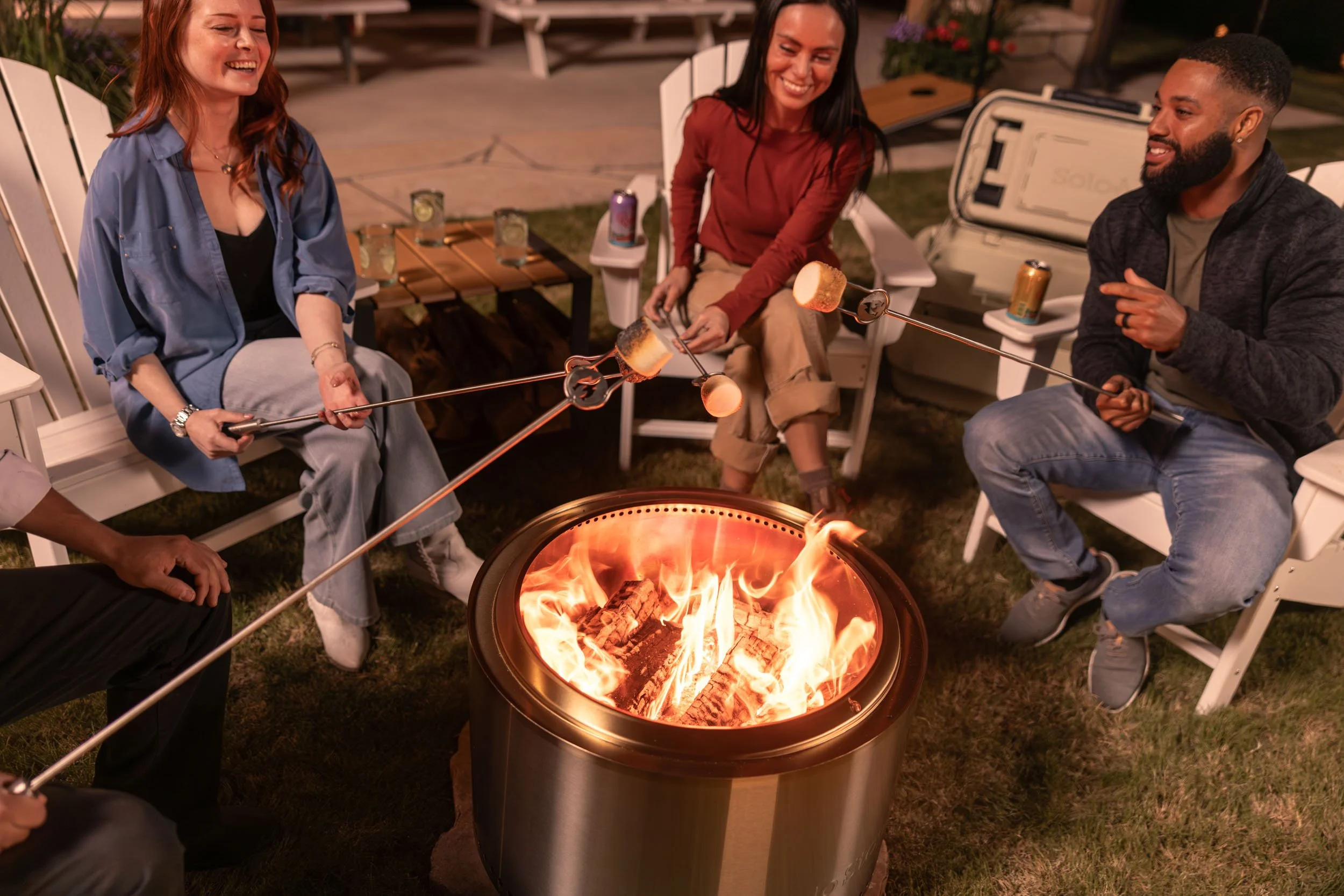 Group of friends sitting around a fire pit roasting marshmallows during a backyard evening gathering.
