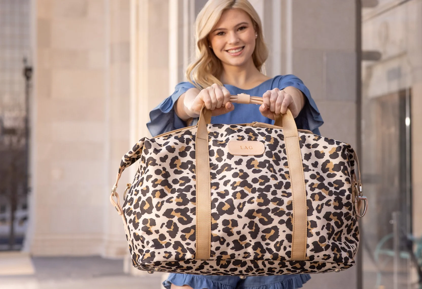 A woman holding a large leopard print bag outdoors with a smile.
