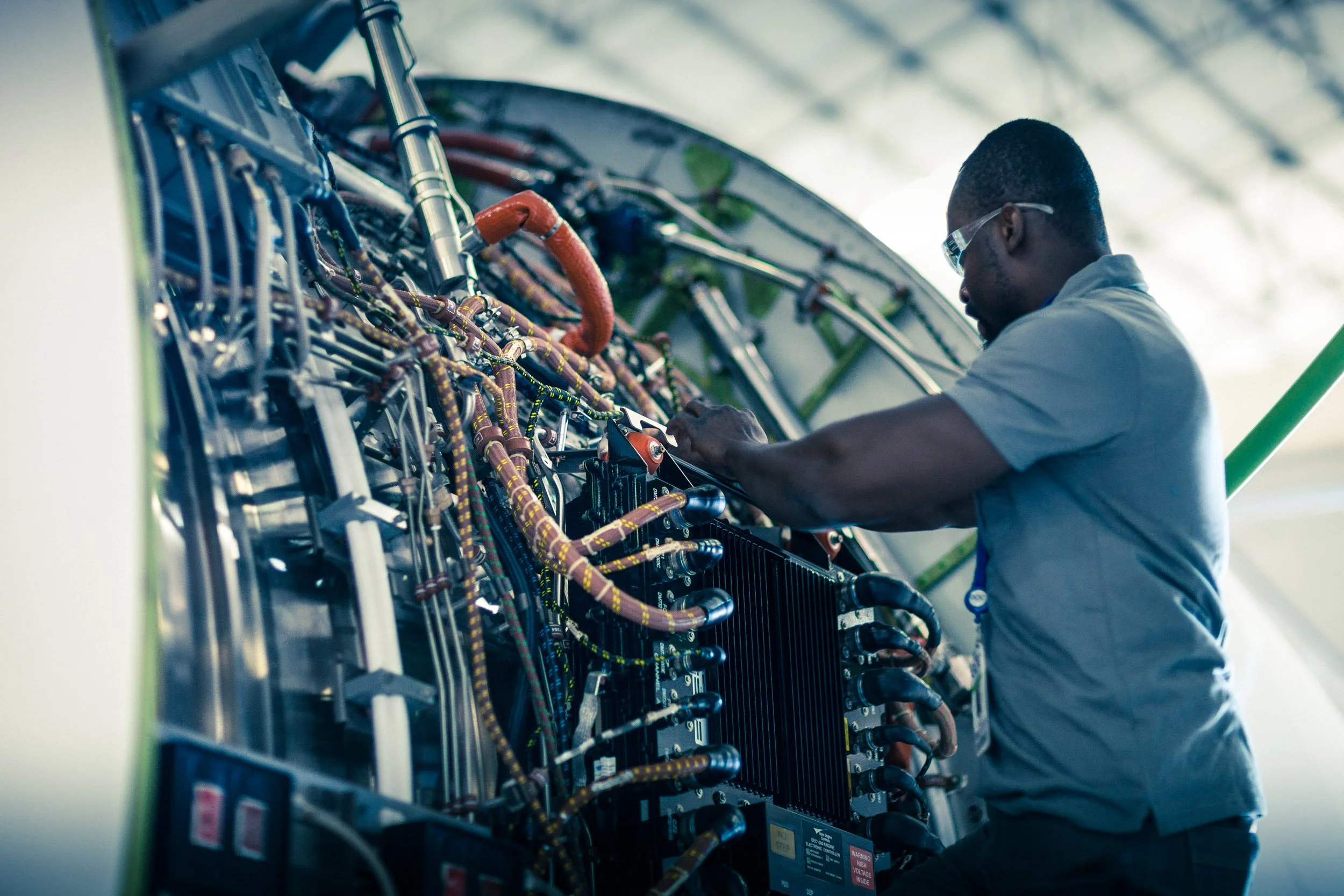 A technician working on electrical components inside a large equipment panel or circuit box, wearing safety glasses.