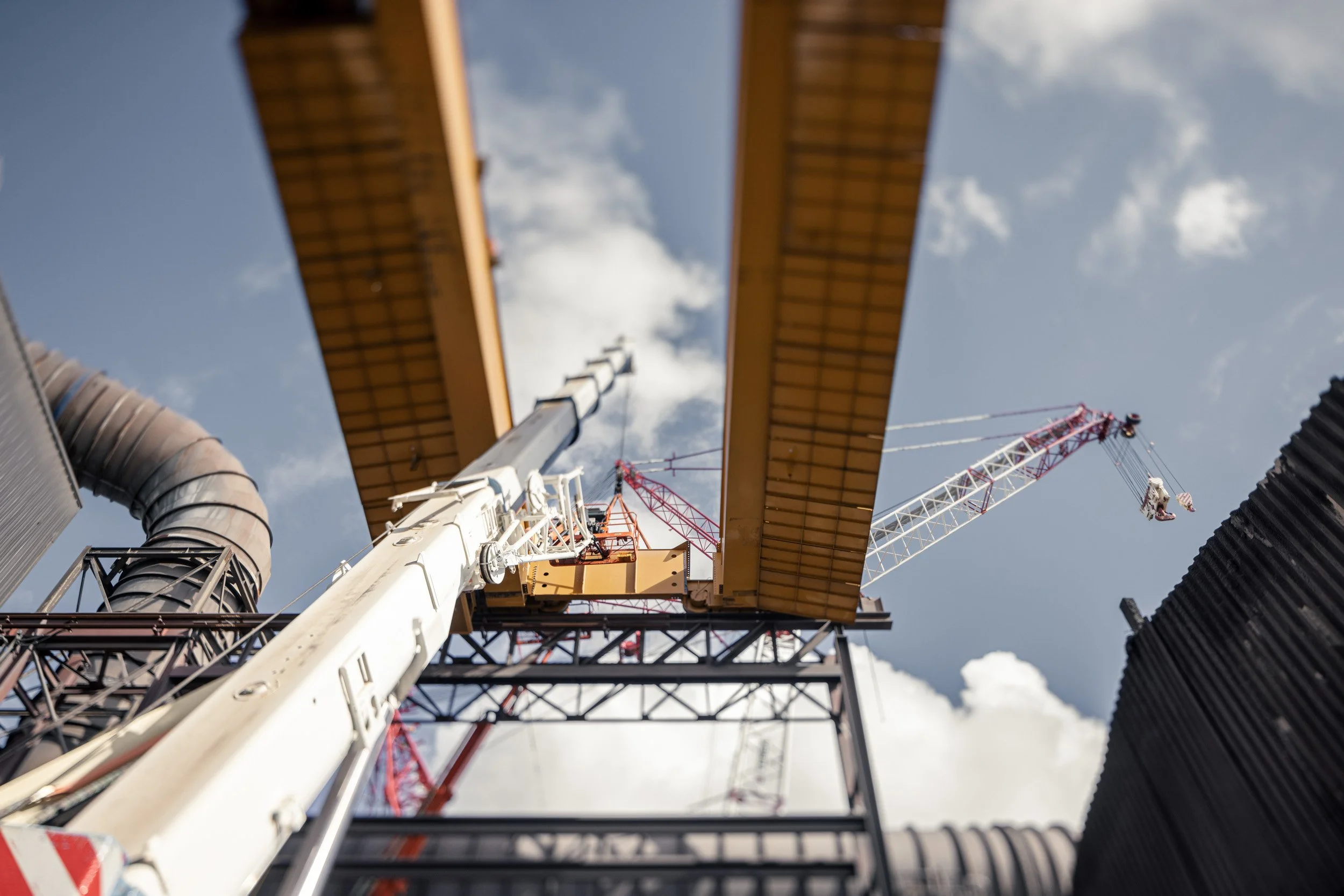 A construction crane lifting a large yellow beam in the sky during daytime.