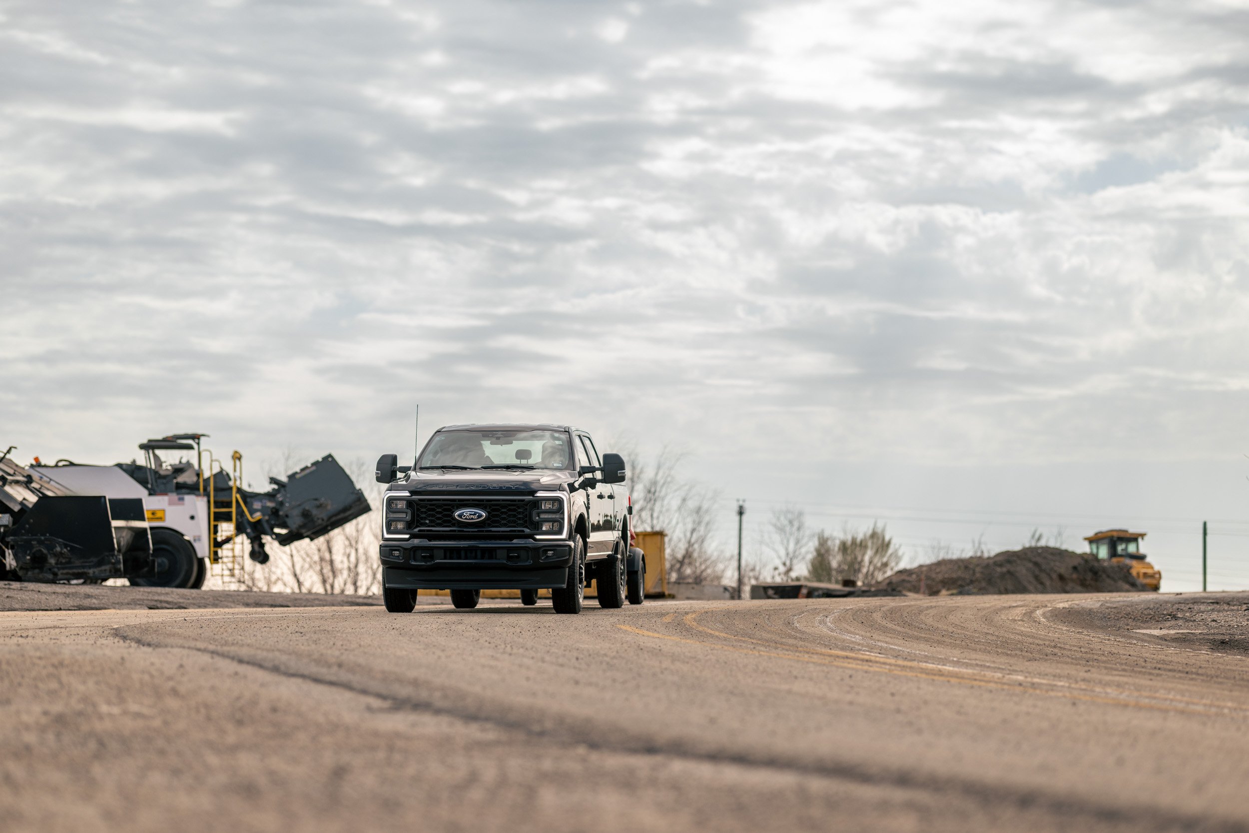A black Ford pickup truck parked on a dirt lot with construction machinery and equipment in the background, under a cloudy sky.