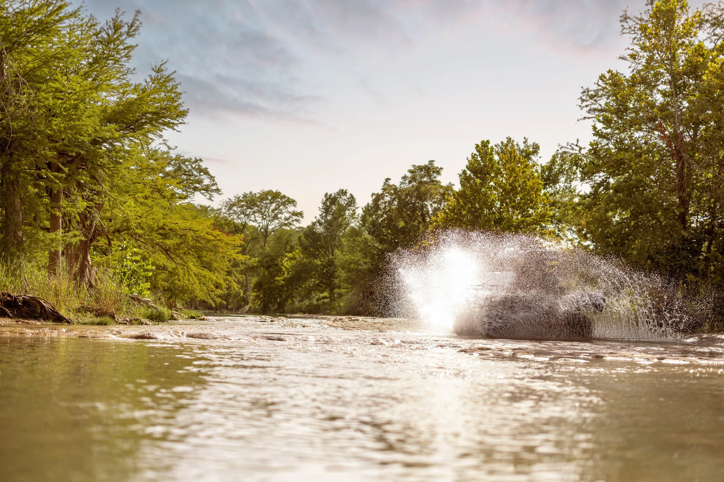 A river with trees on both sides and a splash of water from something hitting the water, with a partly cloudy sky above.