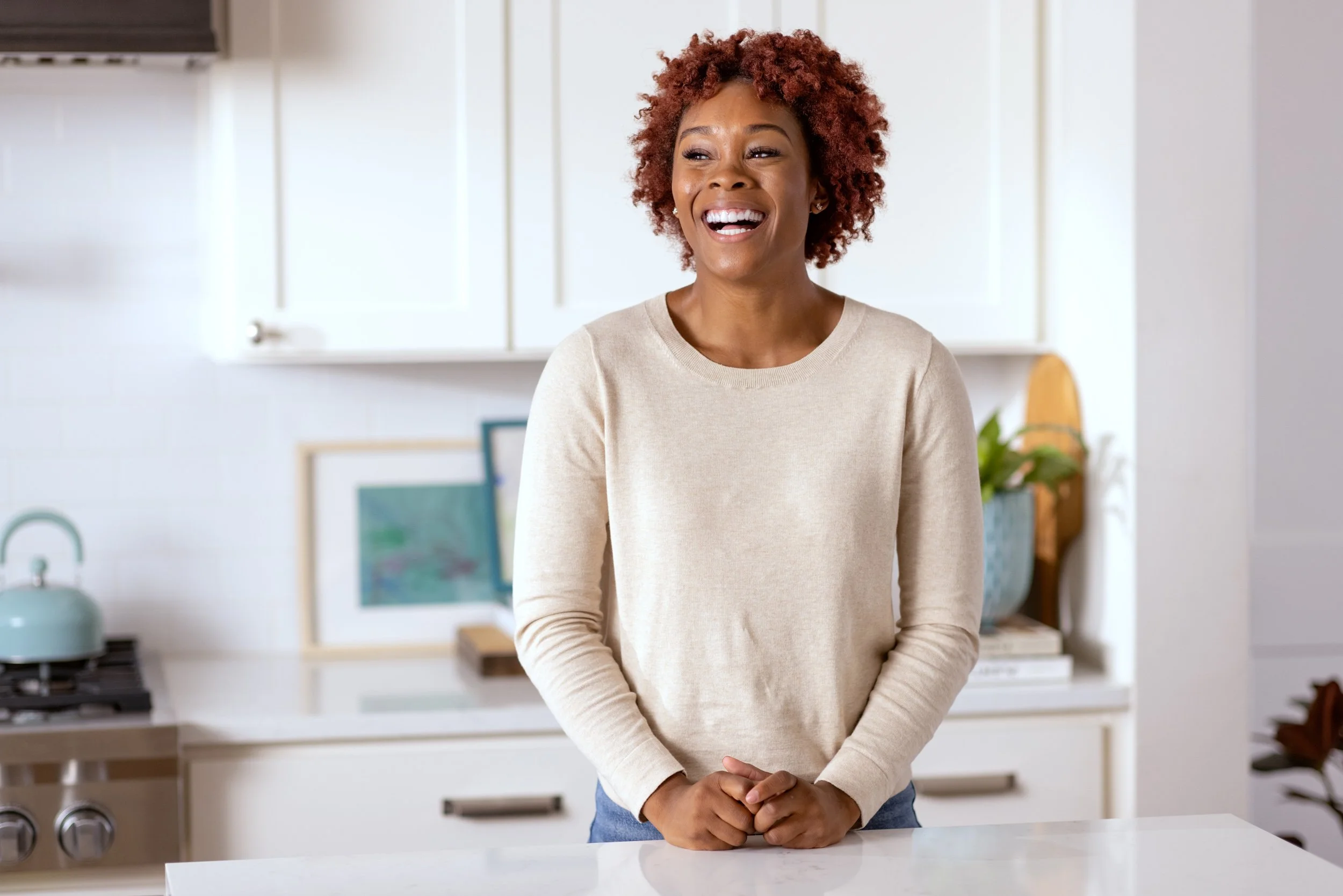 Woman with curly hair smiling in a bright kitchen.