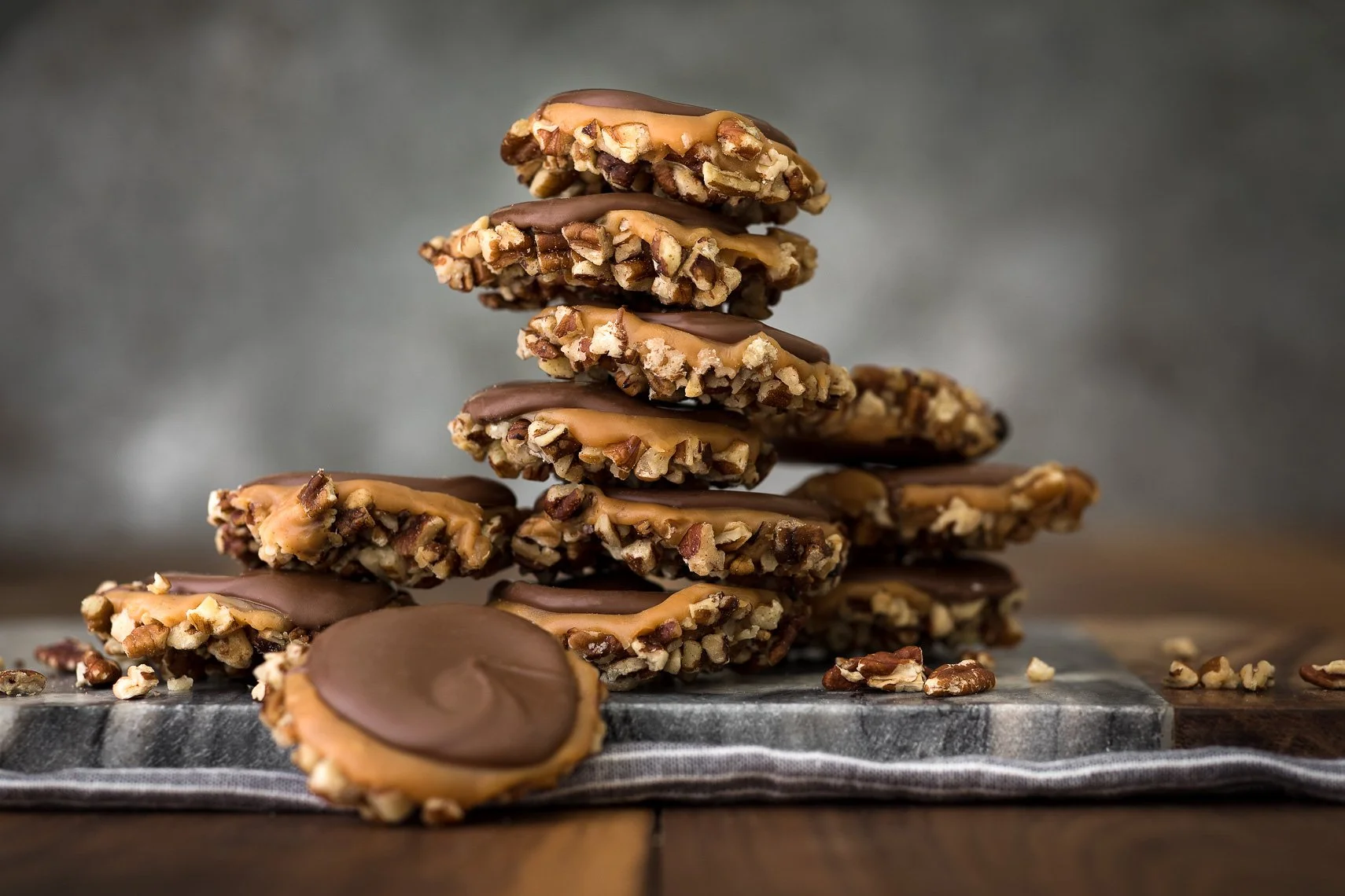 Stack of chocolate-covered peanut caramel cookies on a dark wooden surface.